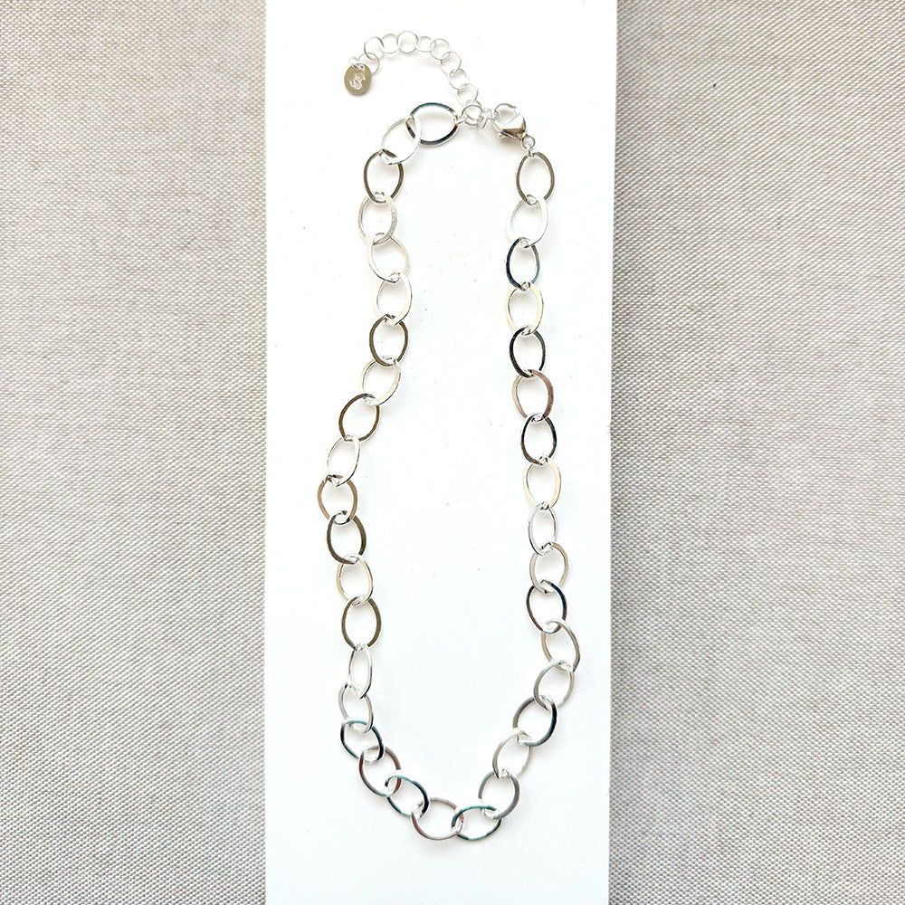 Chunky silver chain necklace on a white and beige fabric background