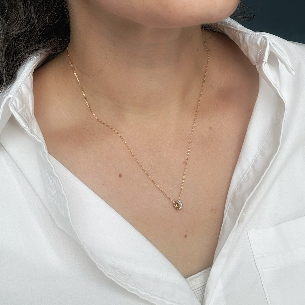 Close up of person wearing Diamond pave wheel charm on a gold chain