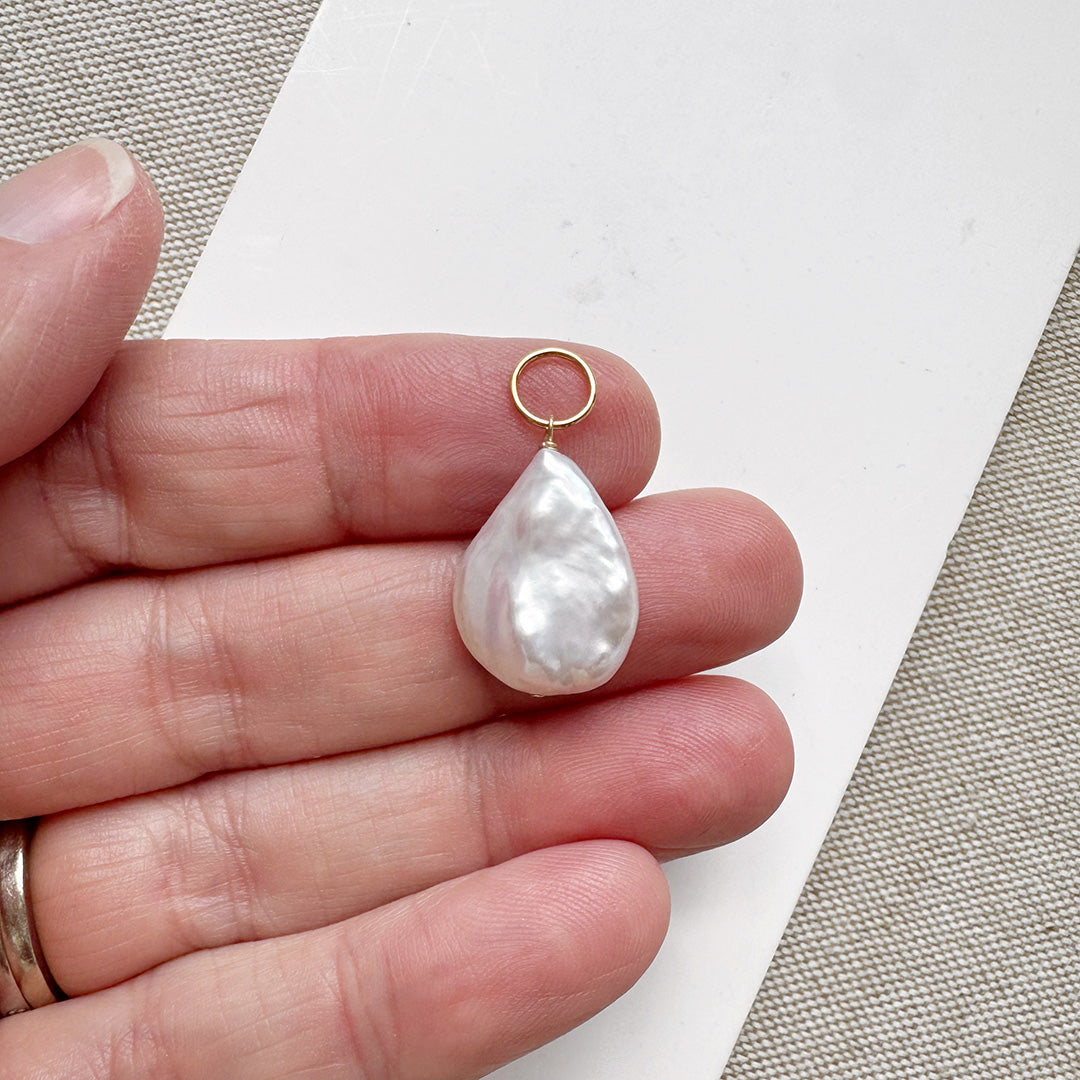 Hand holding a tear drop shaped pearl charm
