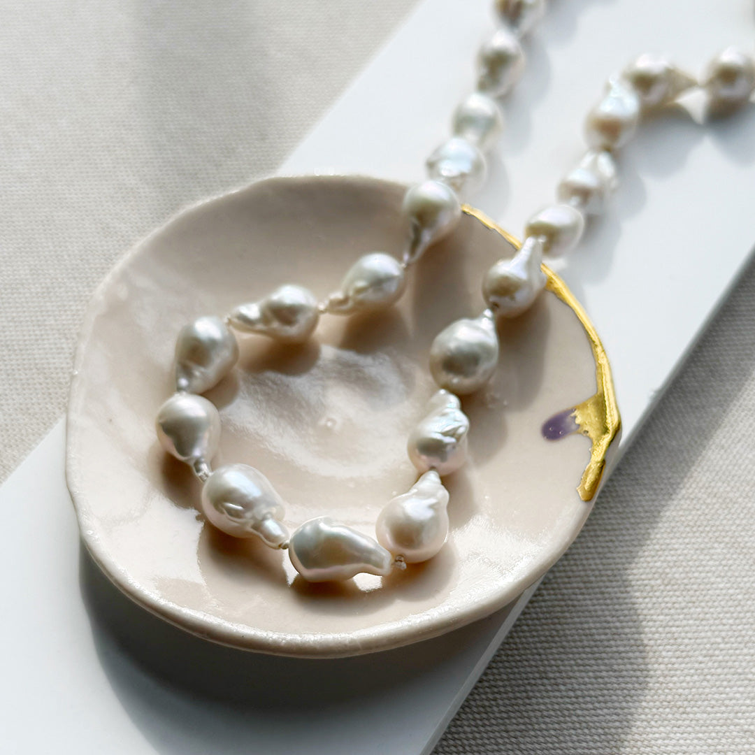 Baroque pearl necklace on a ceramic dish with a white background
