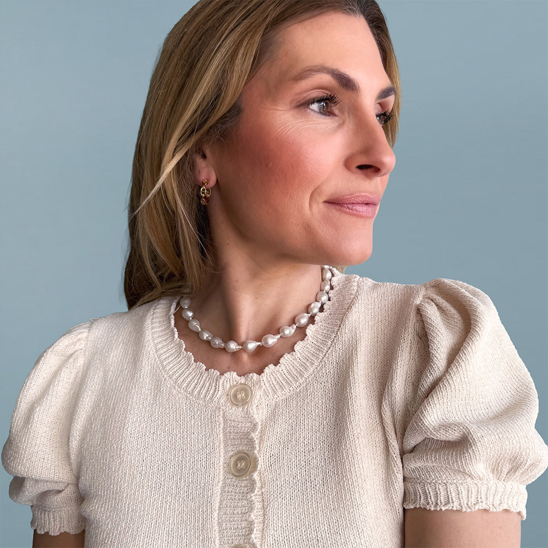 Woman wearing a beige cardigan and pearl necklace against a light blue background