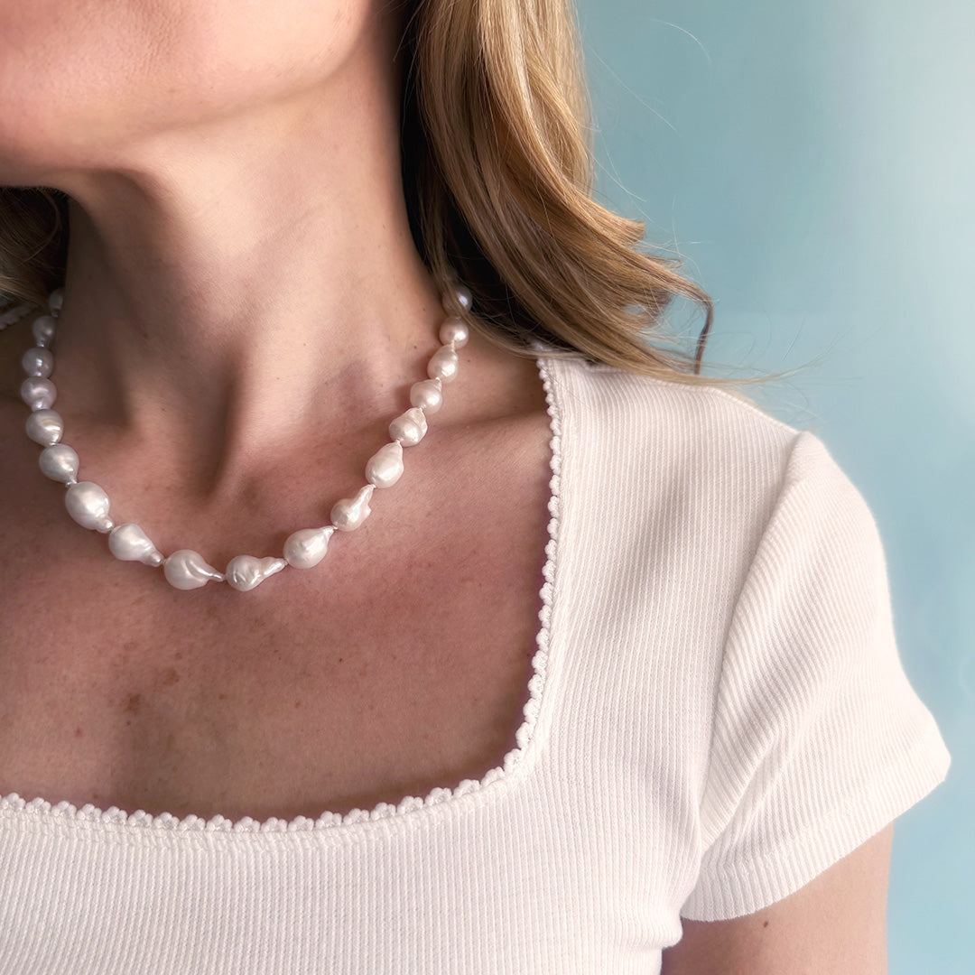Pearl necklace worn by a person against a light blue background