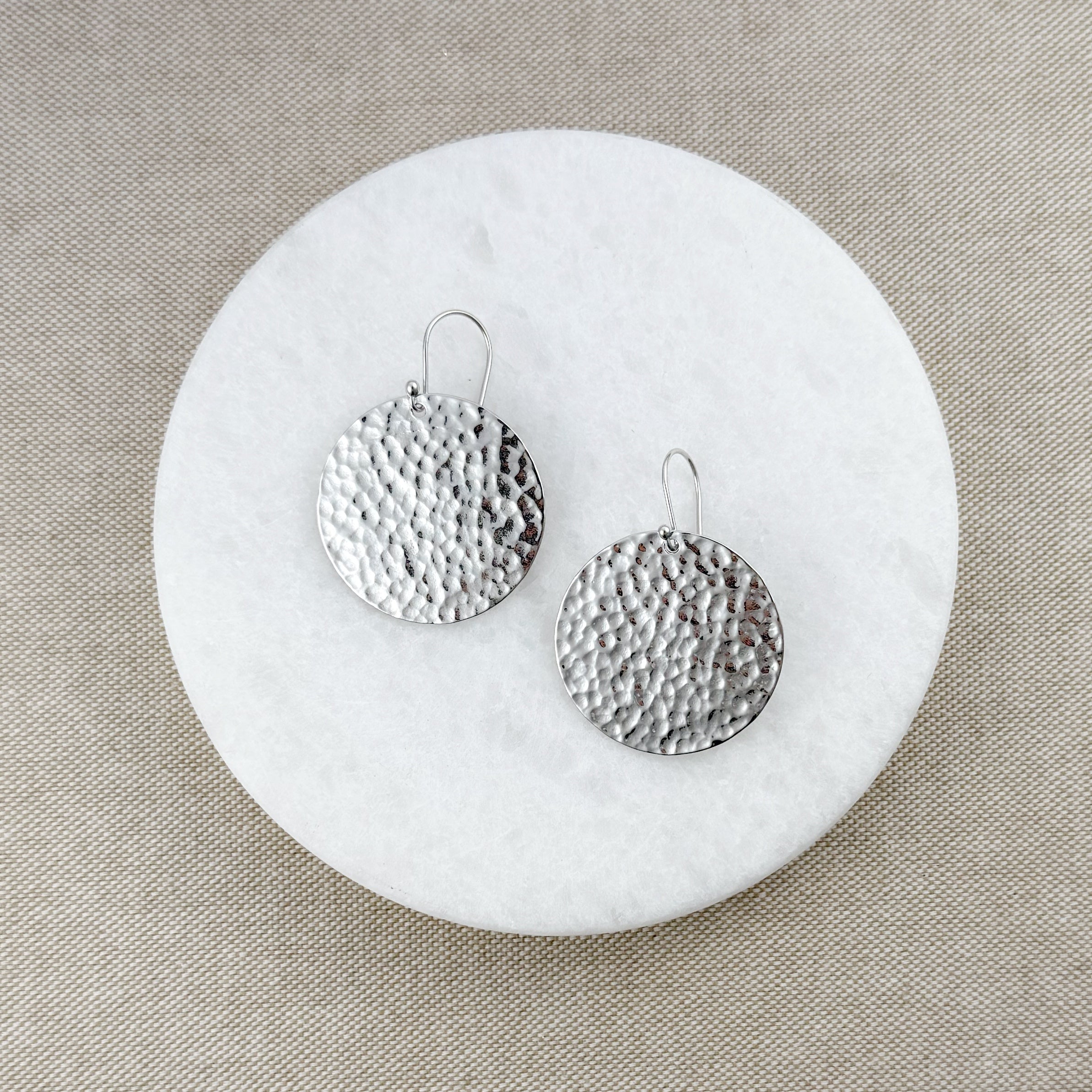 Pair of large round silver earrings on a round marble coaster