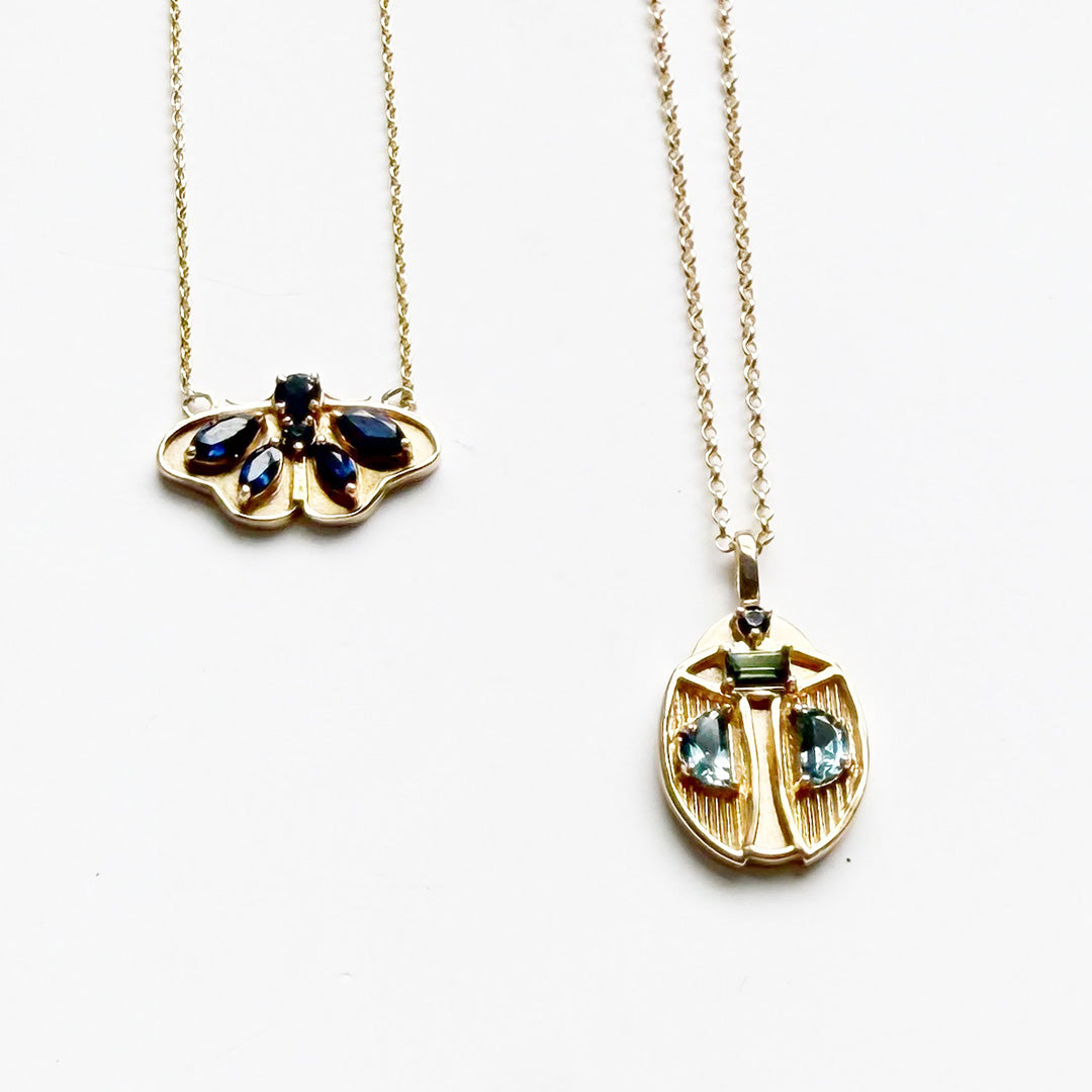 Two gold necklaces with butterfly and beetle pendants on a white surface