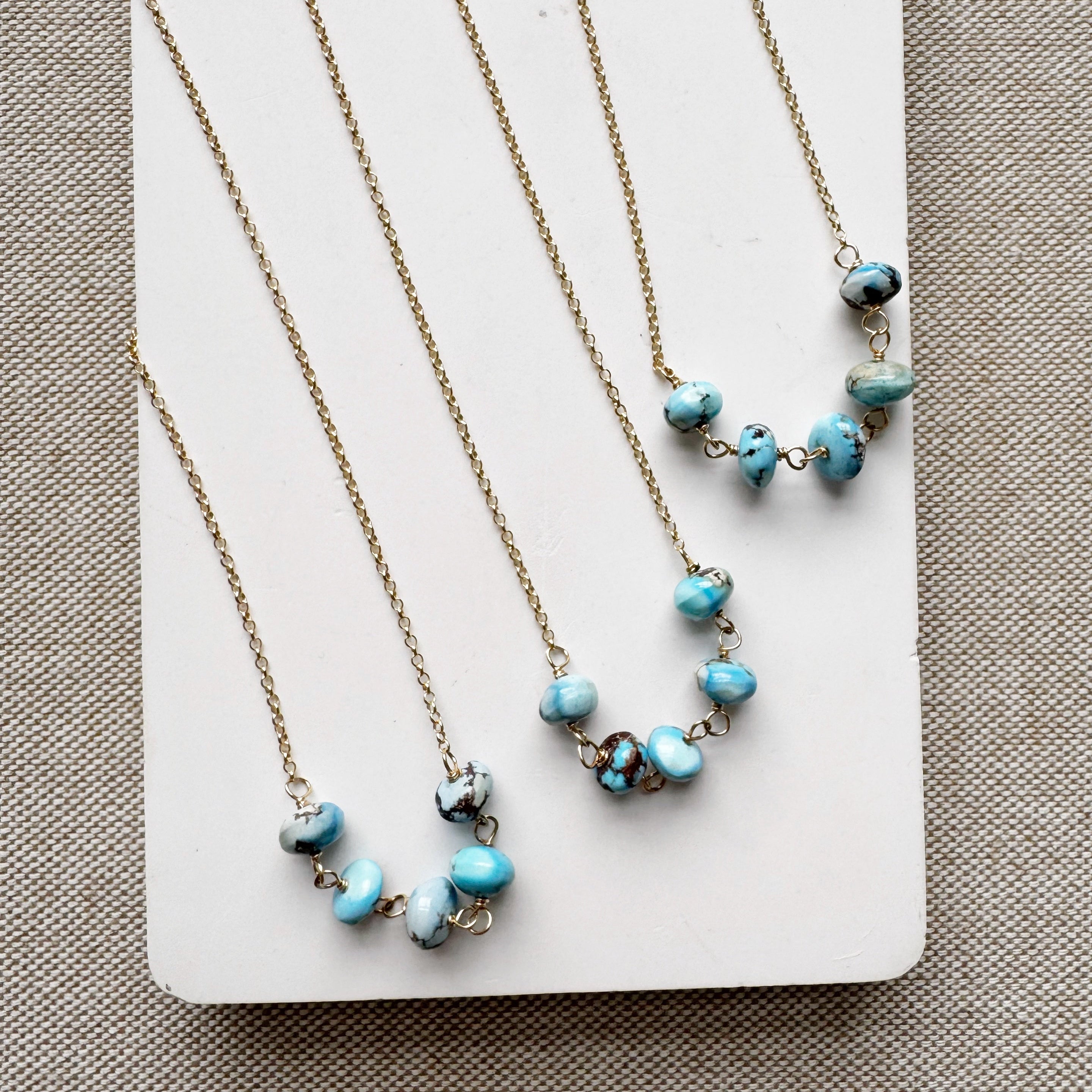 Three gold necklaces with Golden Hill turquoise beads on a white card against a beige background