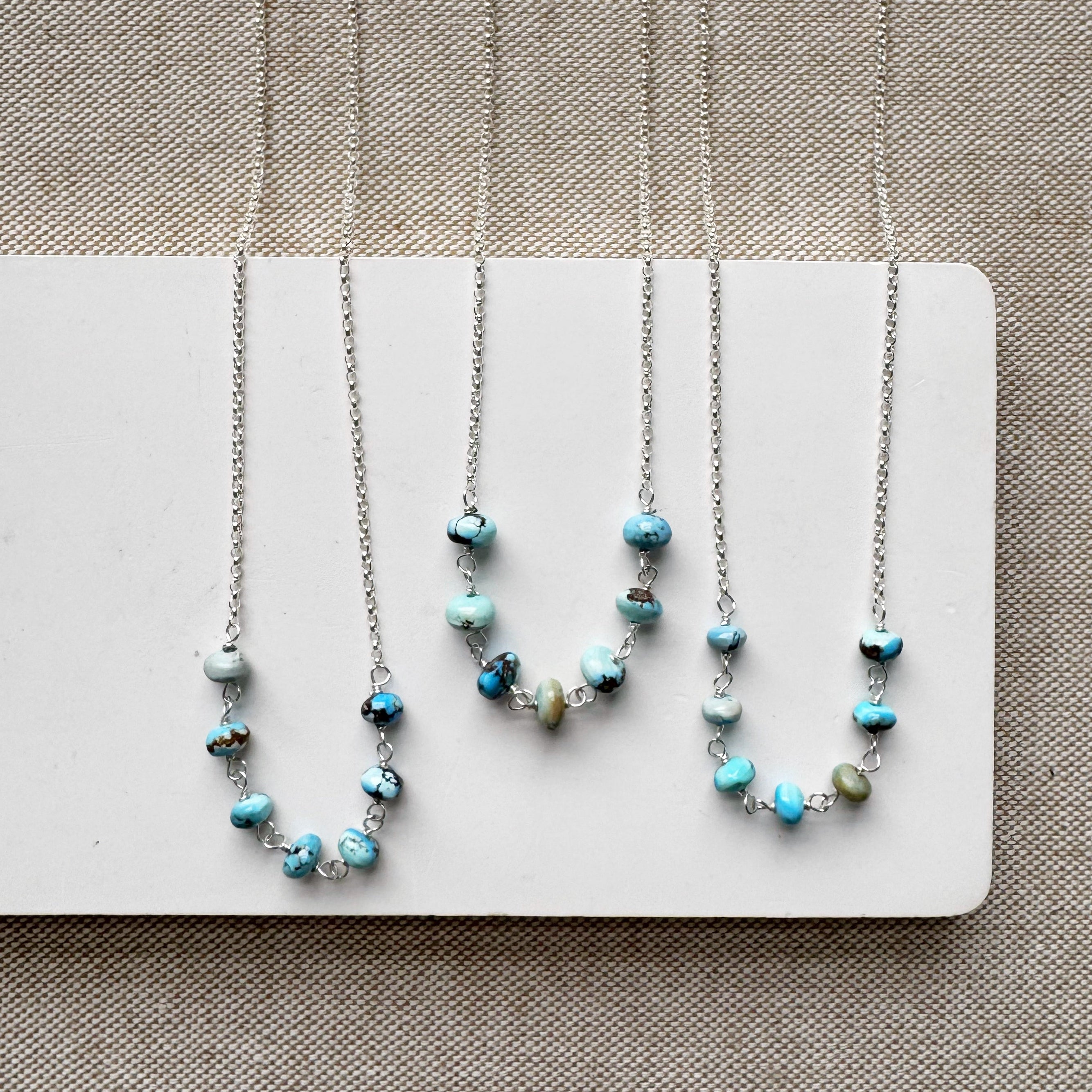 Three silver necklaces with Golden Hills turquoise beads on a white card against a beige background