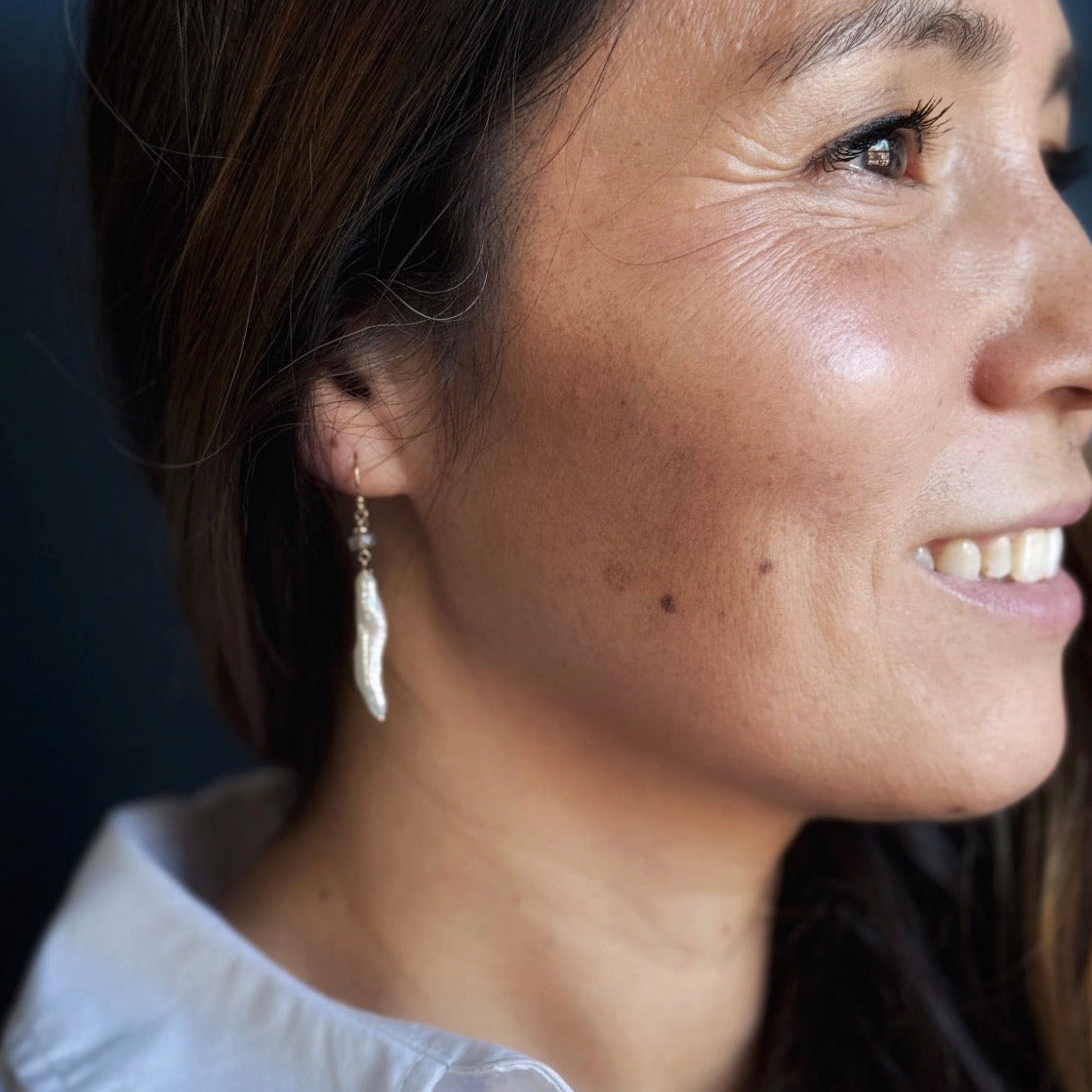 Woman wearing stick pearl earring on a blue background