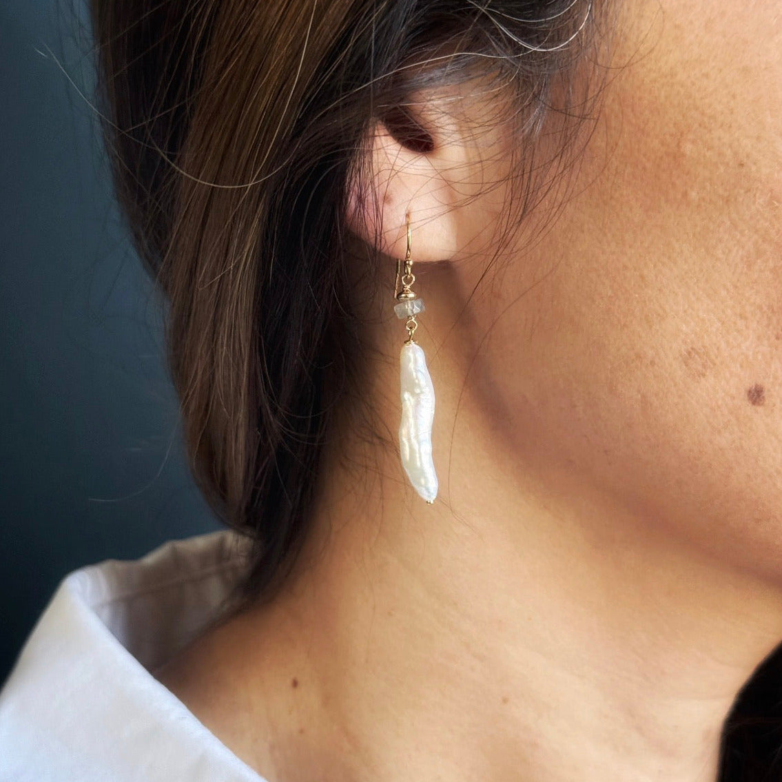 Woman wearing stick pearl earring on a blue background