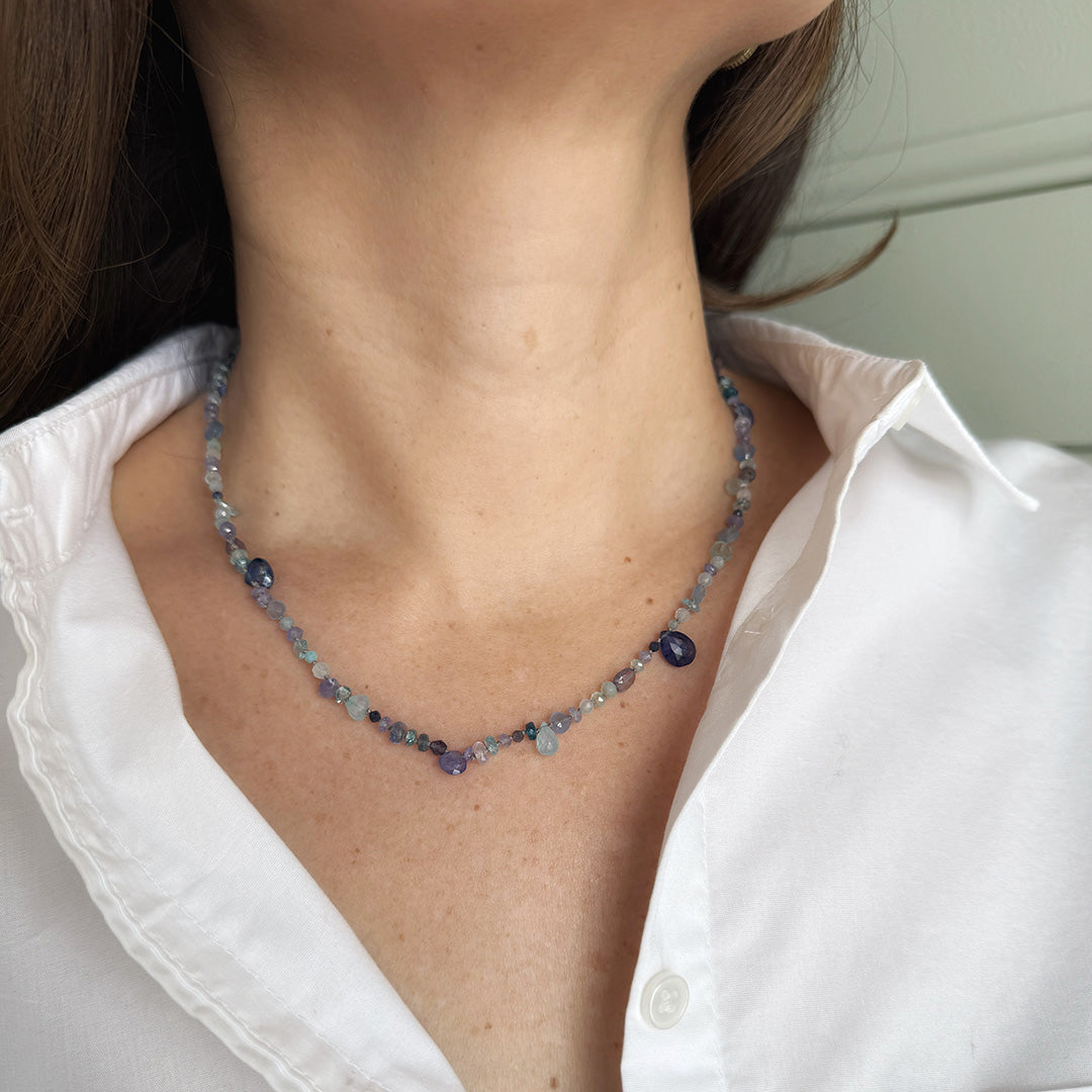 Gemstone necklaces in shades of blue worn by a person in a white shirt.