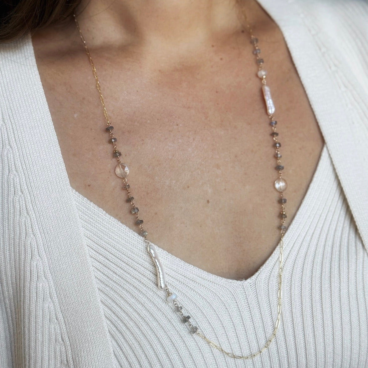 Woman wearing long necklace with labradorite gems and stick pearls on a blue background