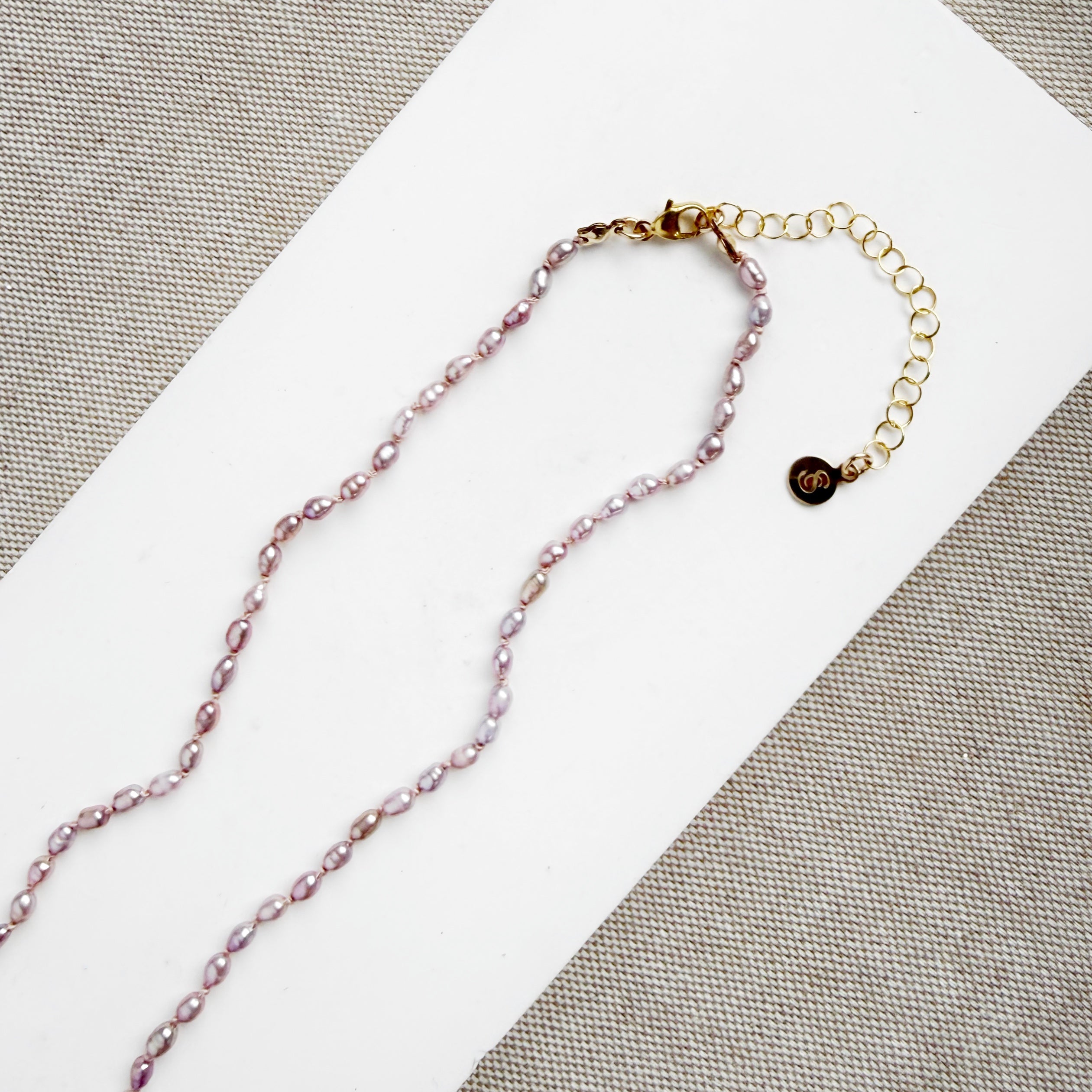 Clasp detail of knotted necklace with tiny pink pearls on a white card