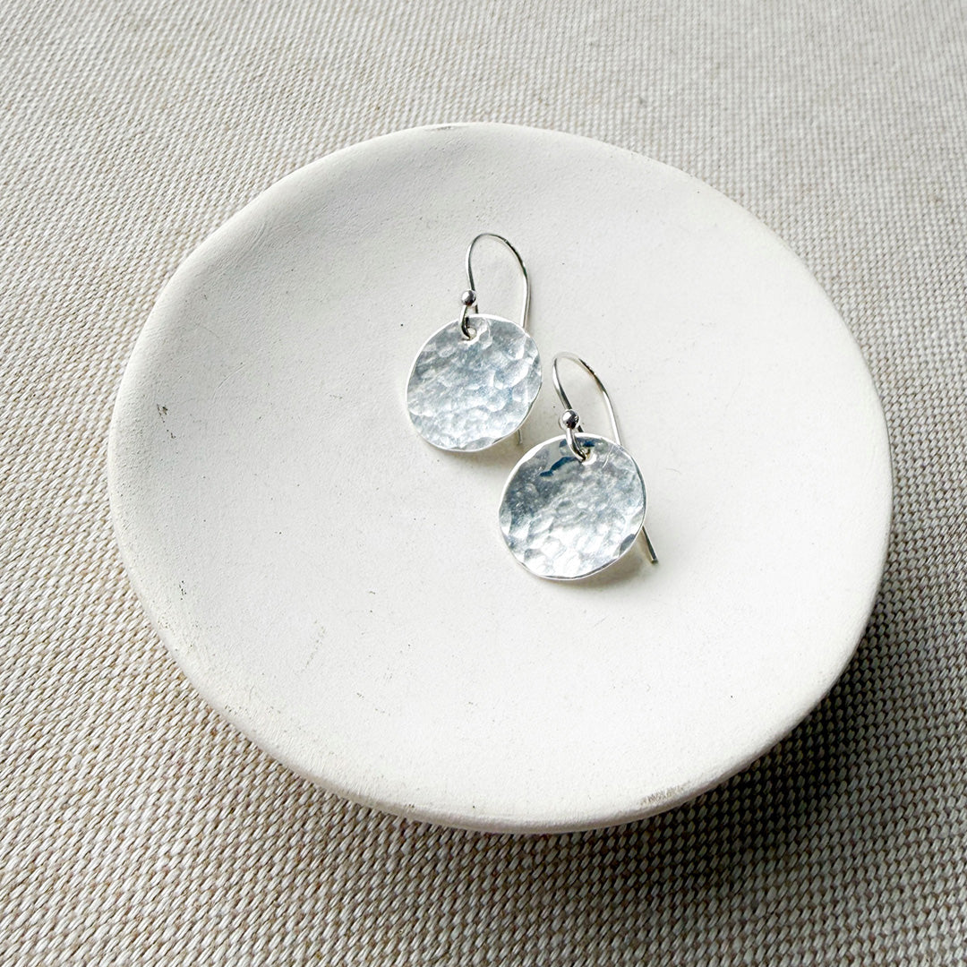 Silver disc earrings on a round white stone surface