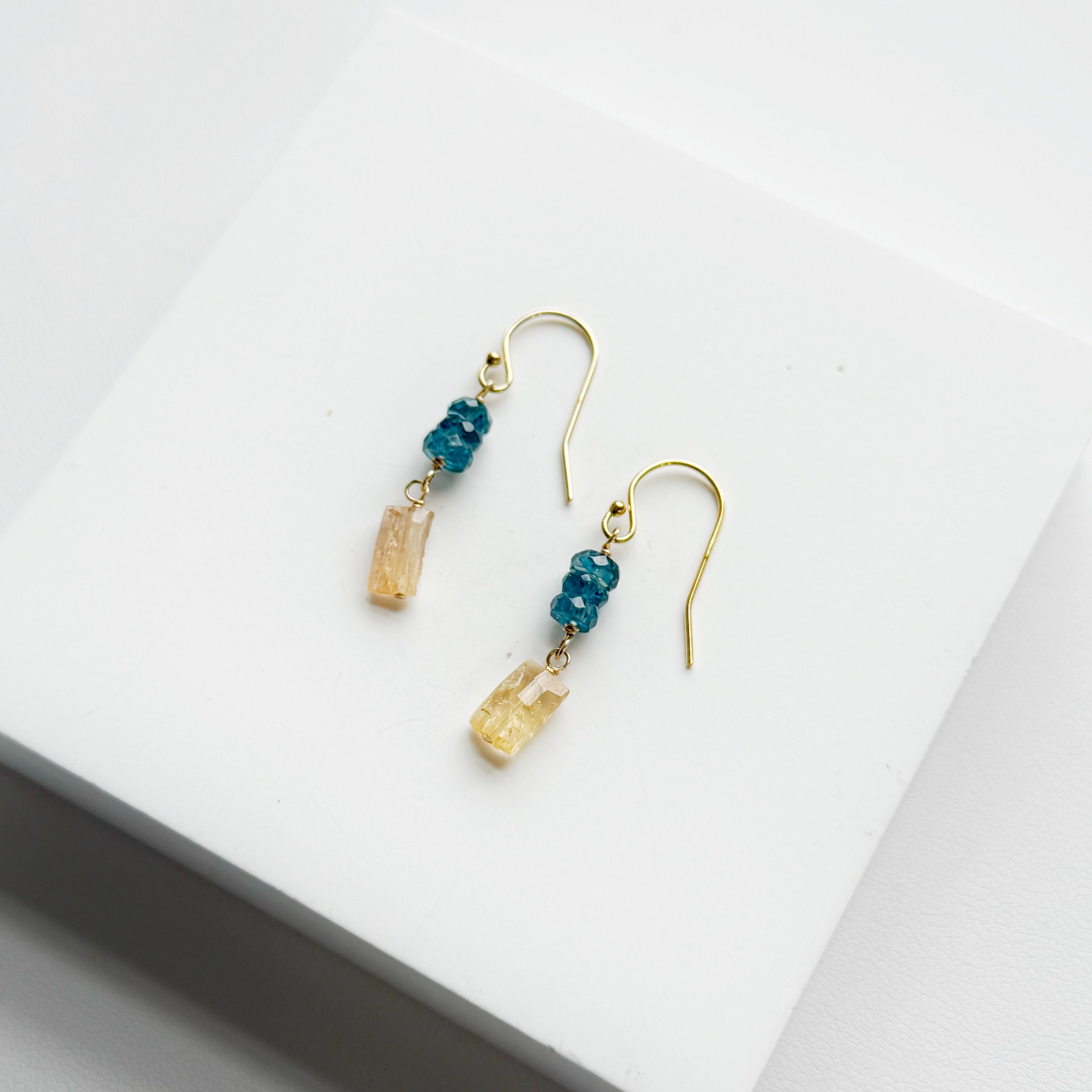 Gold earrings with blue and gold gemstones on a white surface