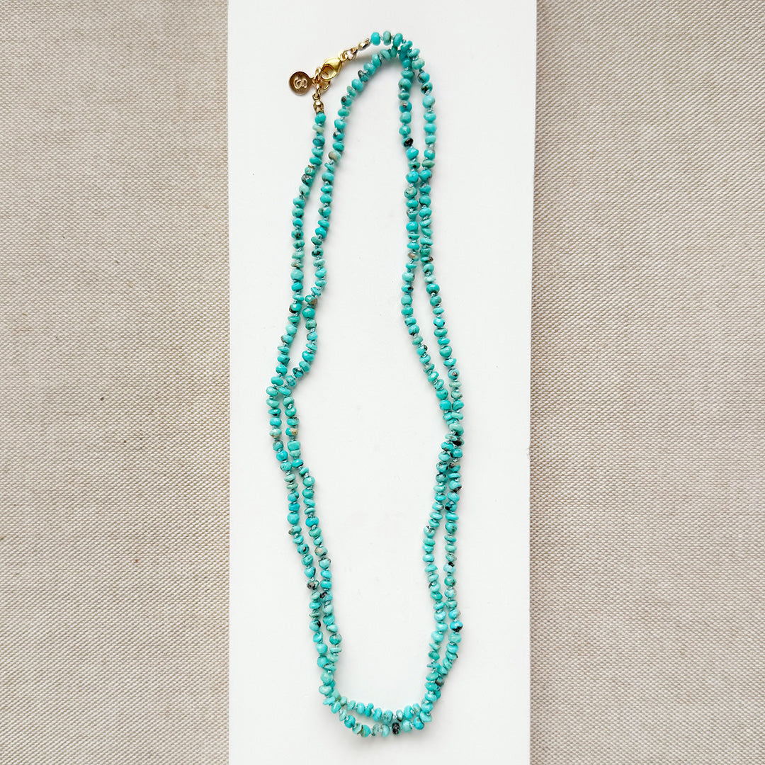 Long turquoise beaded necklace on a beige background