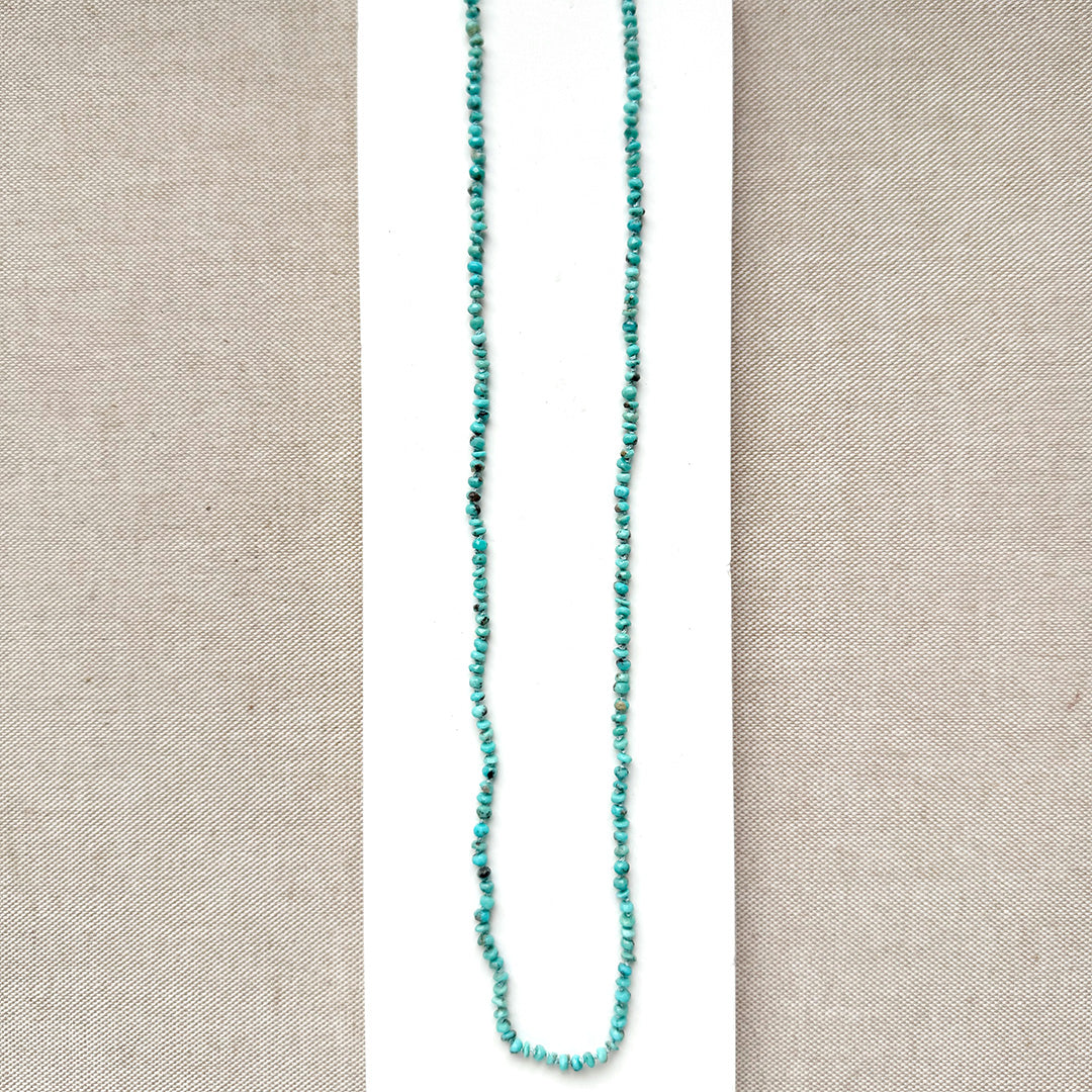 Long turquoise beaded necklace on a beige fabric background
