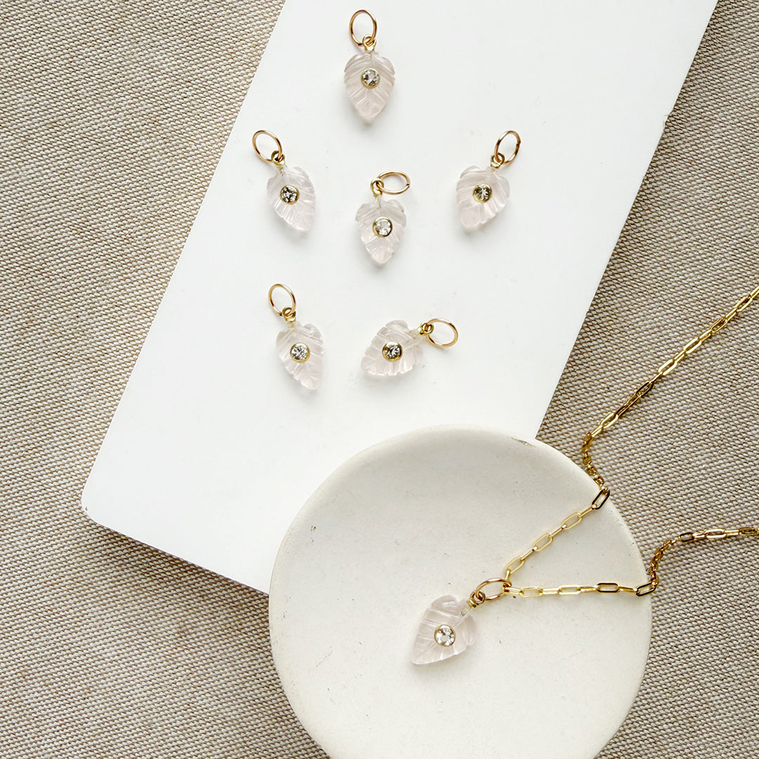 Carved leaf charm in rose quartz on a gold chain in a white dish