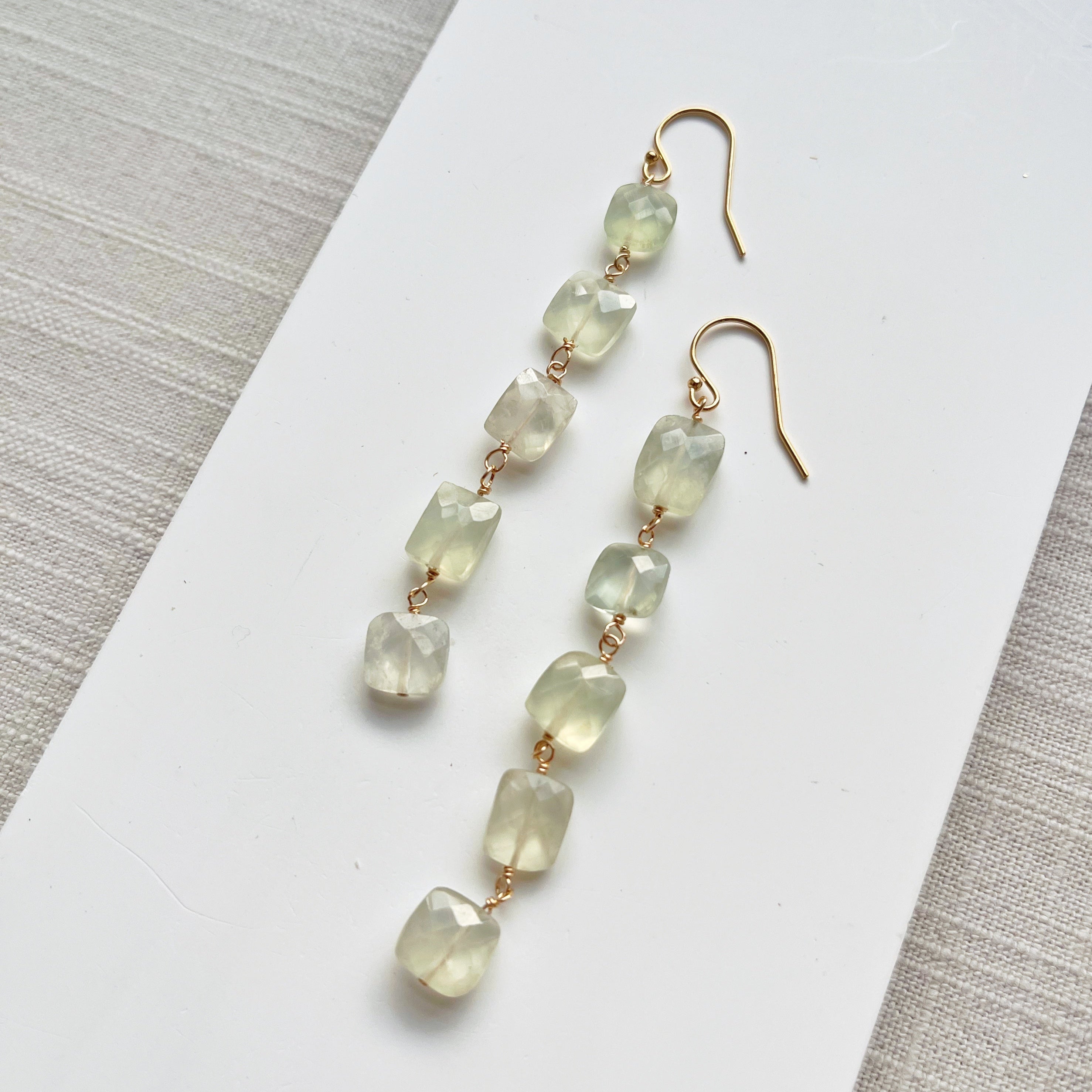 Green beaded earrings on a white card with a gray textured background