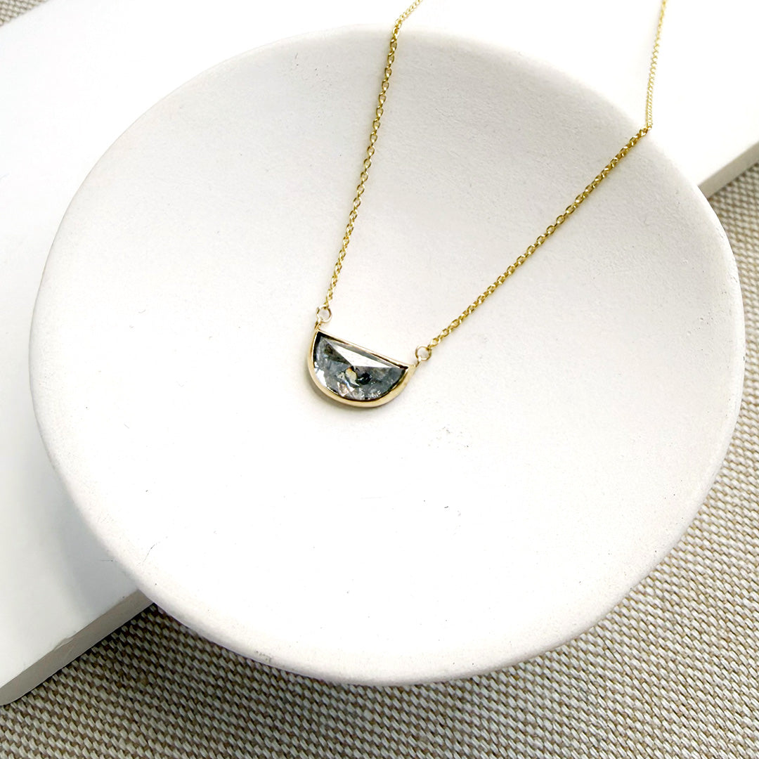 Solid gold necklace with a half moon salt and pepper diamond pendant in a white dish
