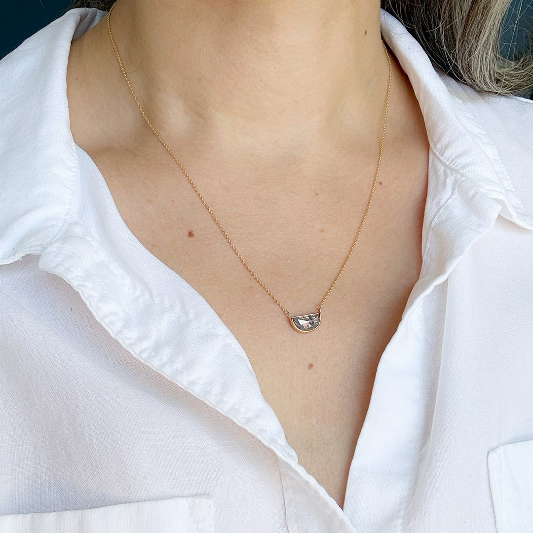 Person wearing solid gold necklace with a half moon salt and pepper diamond pendant.