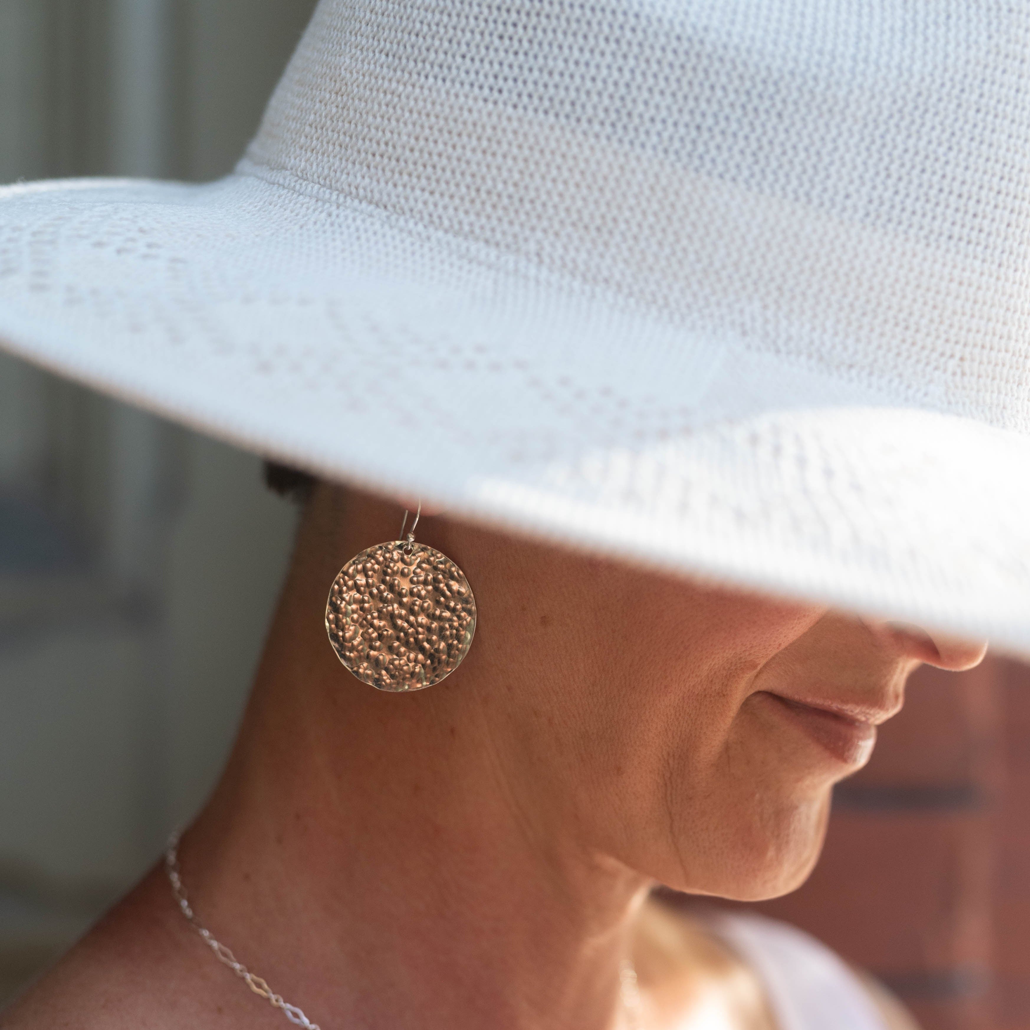Woman in white hat wearing large gold disc statement earrings