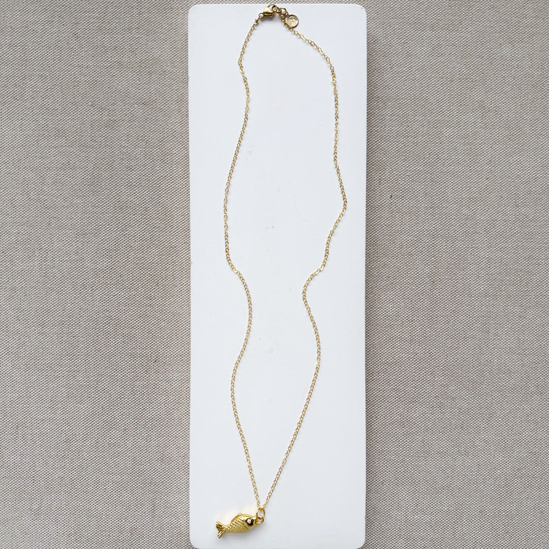 Gold fish-shaped pendant on a chain against a beige background