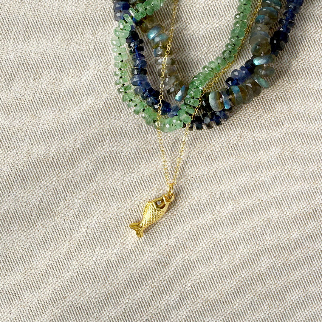 Gold necklace with a fish pendant on a beige fabric background