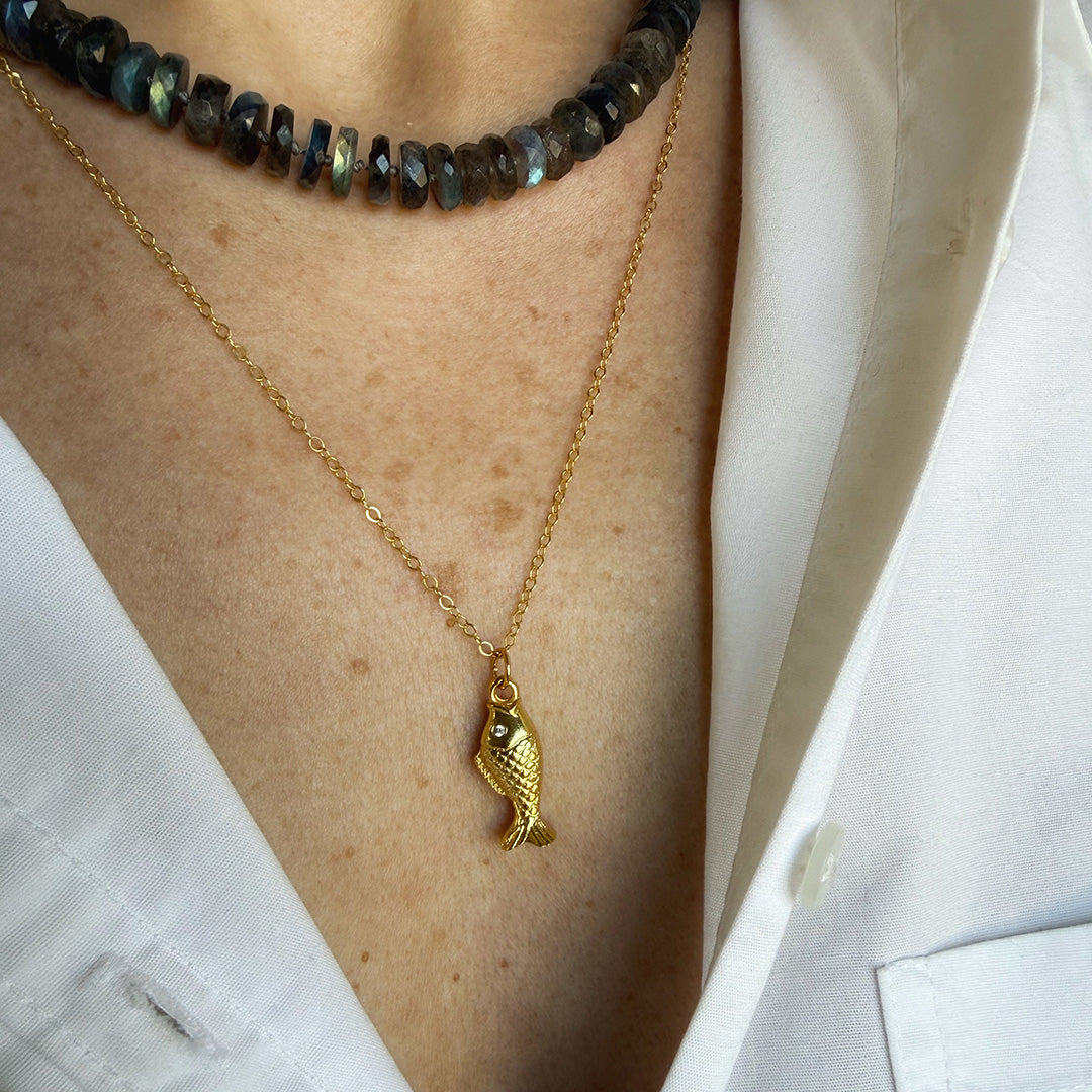 Gold fish pendant necklace on a person wearing a white shirt