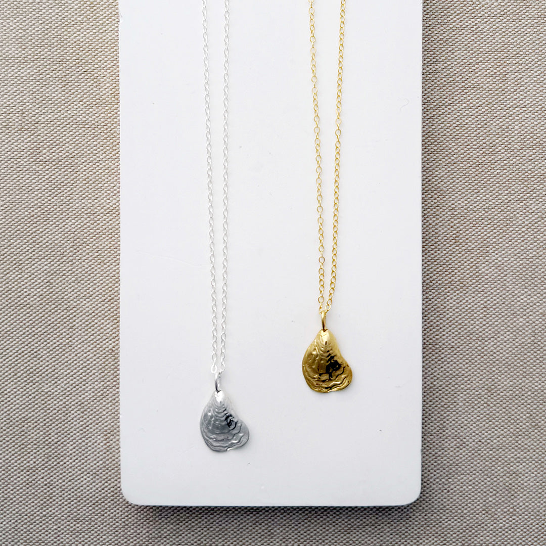 Two necklaces with seashell pendants, one gold and one silver, on a white card.