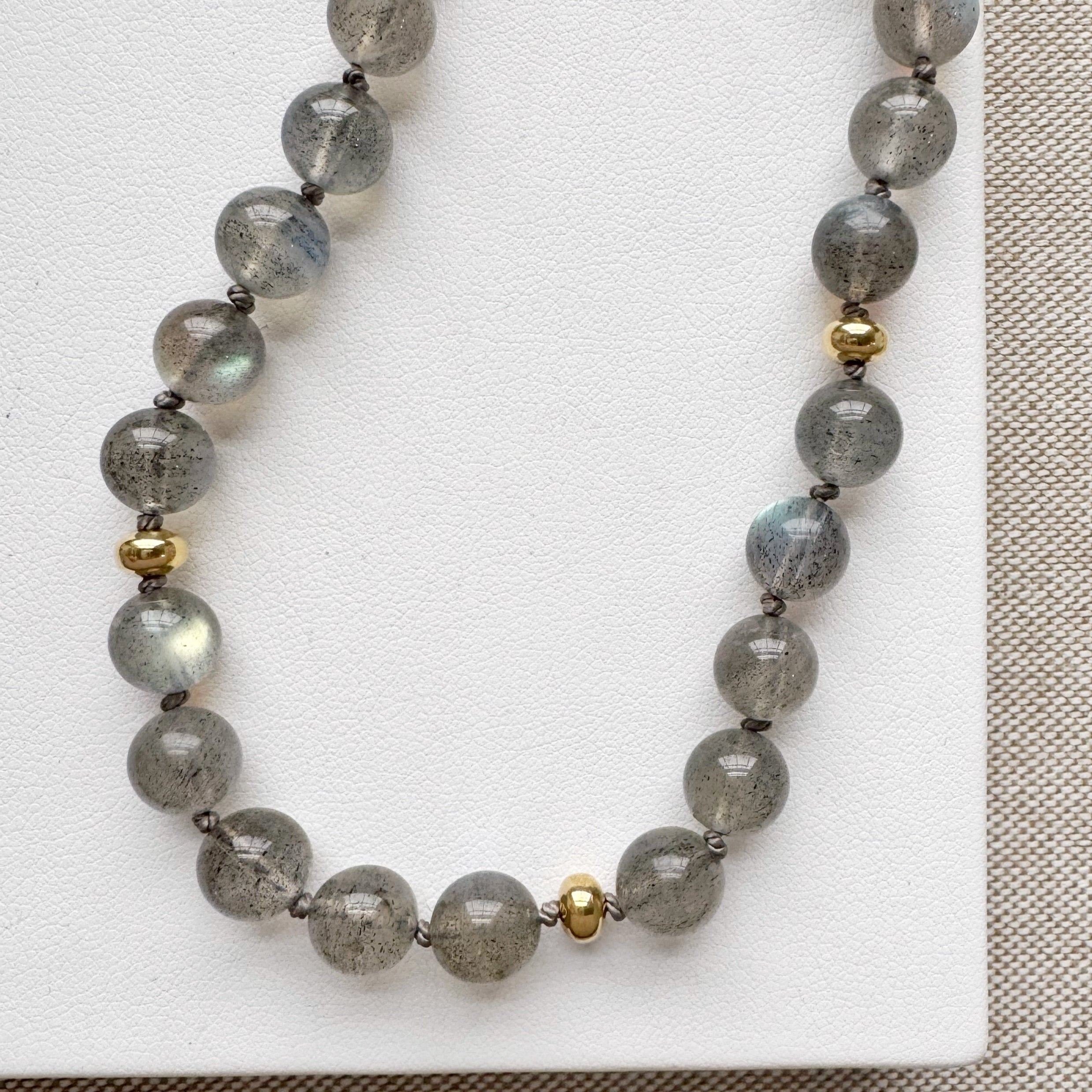A necklace with round labradorite gemstones, featuring gold disc bead accents and a handmade clasp, knotted on silk, displayed on a white surface.