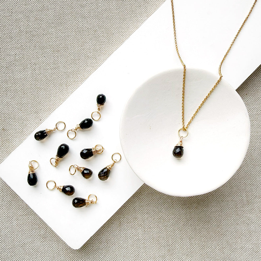 Smokey Quartz charm on a gold chain in a white dish