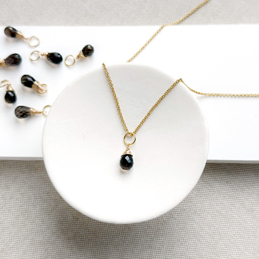 Smokey Quartz charm on a gold chain in a white dish