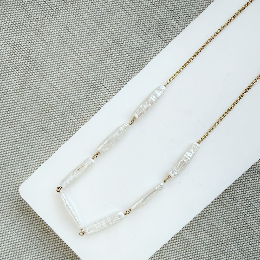 Stick pearl and gold chain necklace on a white background
