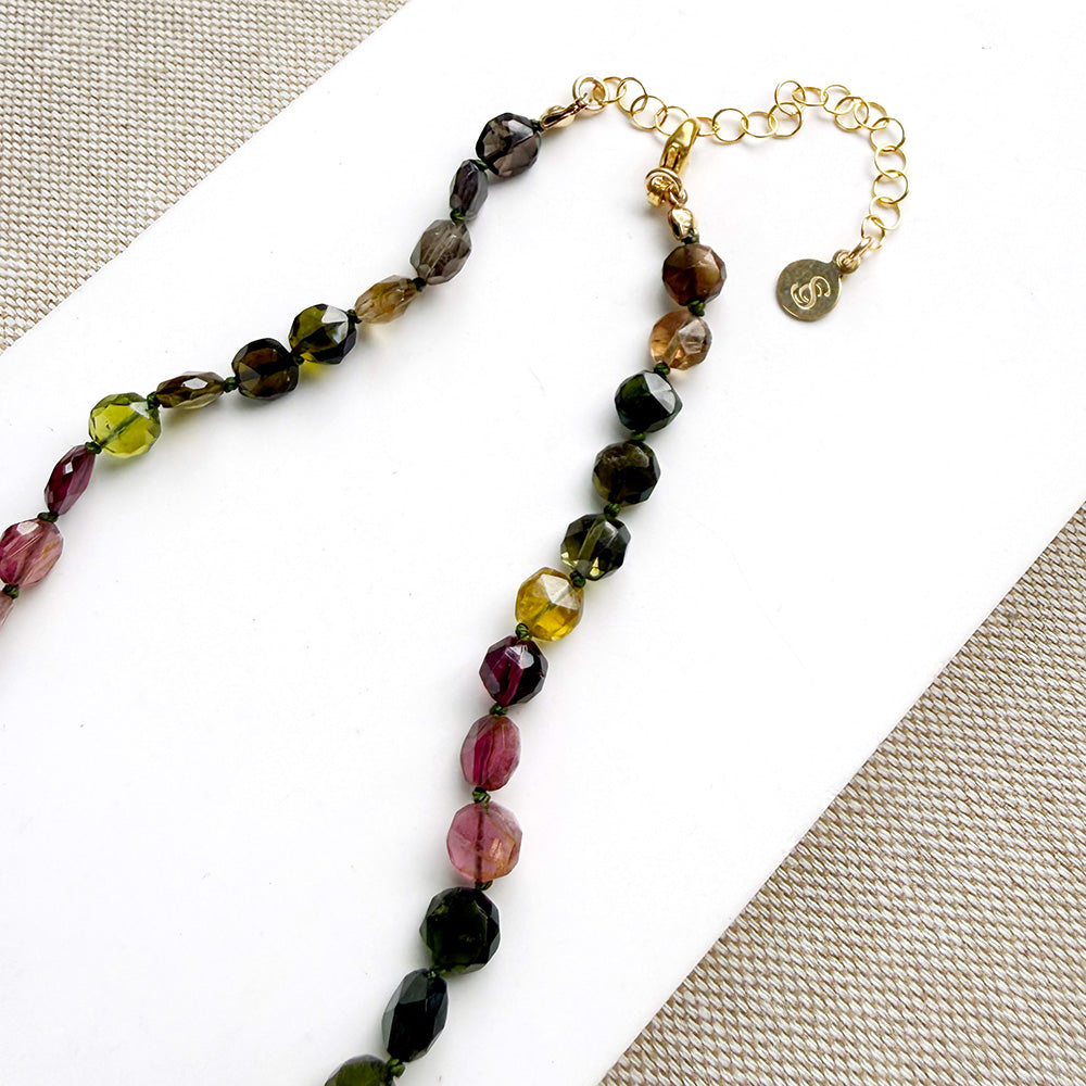 Clasp detail of a necklace with faceted Watermelon Tourmaline gemstone beads in a multicolor mix of green, pink, and blue, on a white surface with textured beige fabric in the background