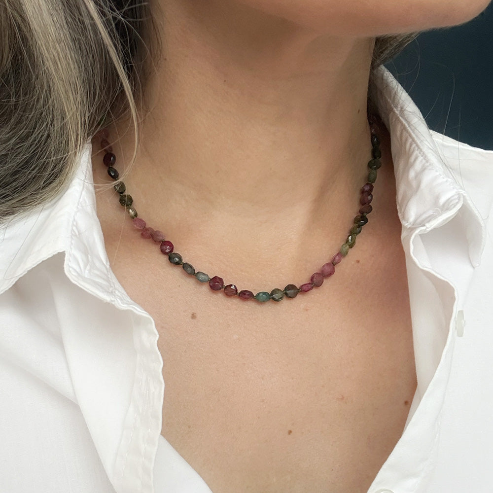 Close up of person wearing a necklace with faceted Watermelon Tourmaline gemstone beads in a multicolor mix of green, pink, and blue, with a white shirt