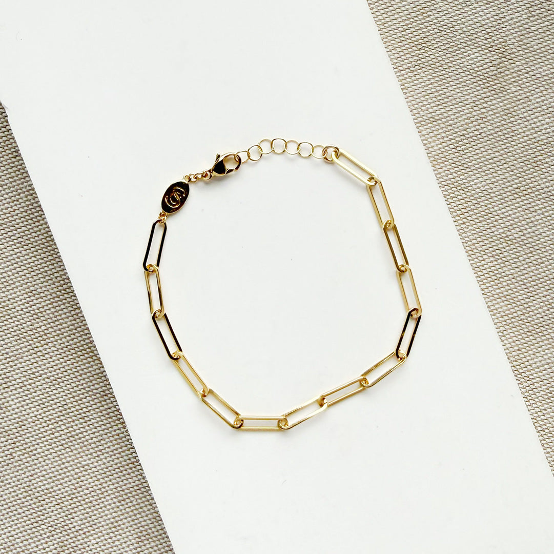 Gold paperclip chain bracelet on a white surface