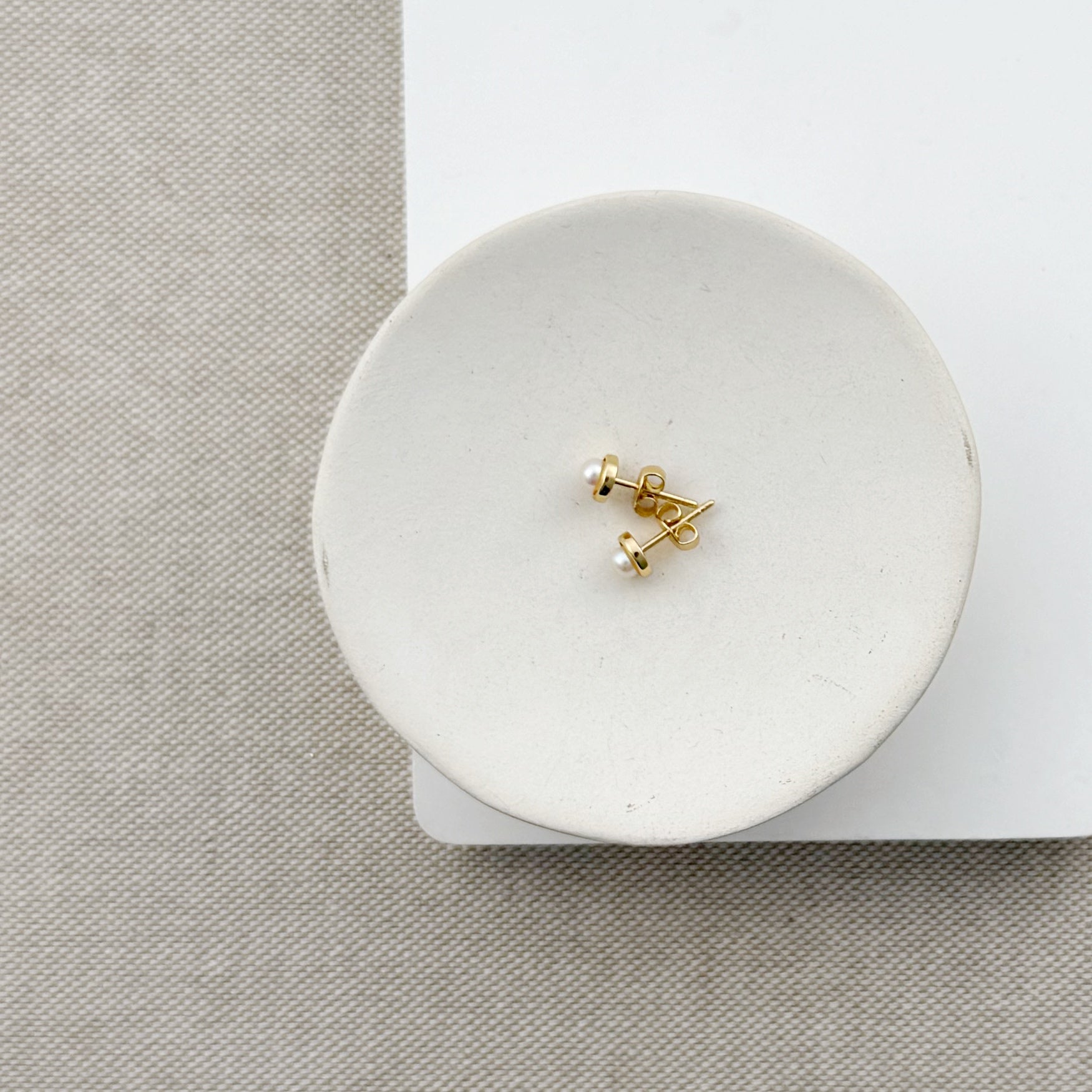 Gold earrings on a white round jewelry dish with a neutral background
