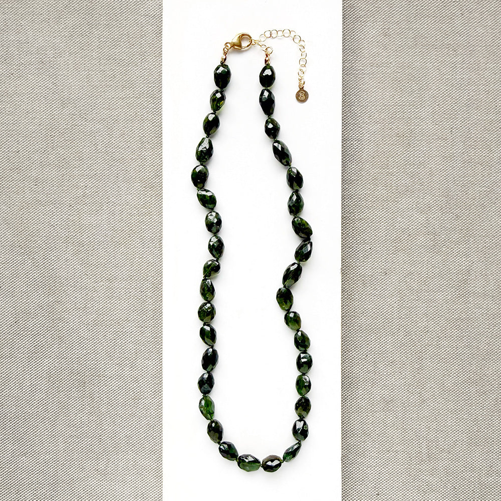 A necklace with faceted Green Tourmaline gemstone beads, on a white surface