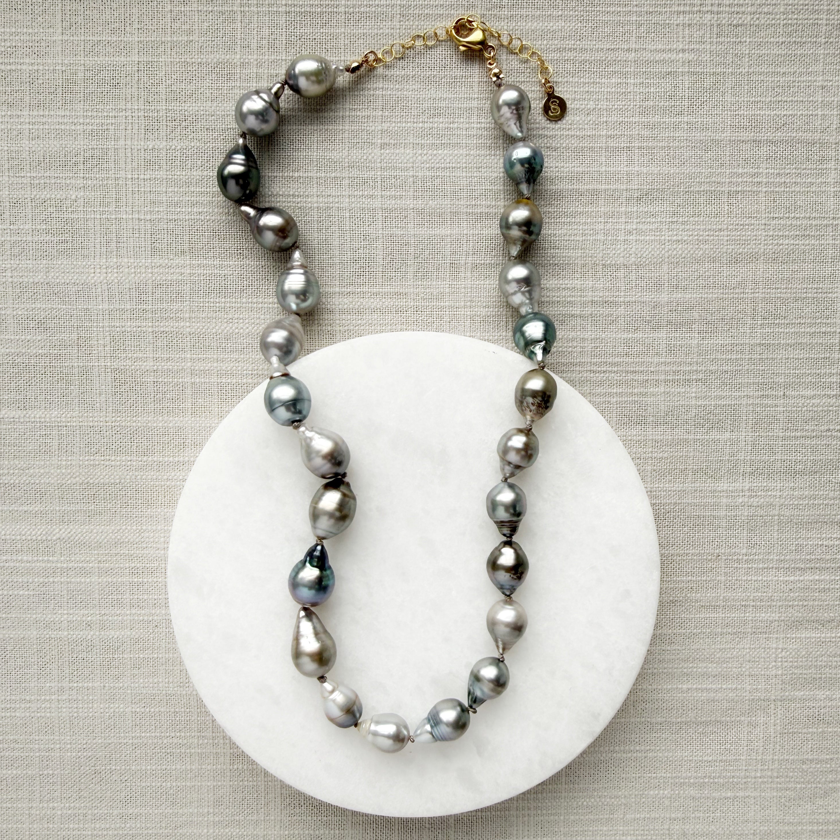Tahitian pearl necklace on a marble coaster with a textured beige background