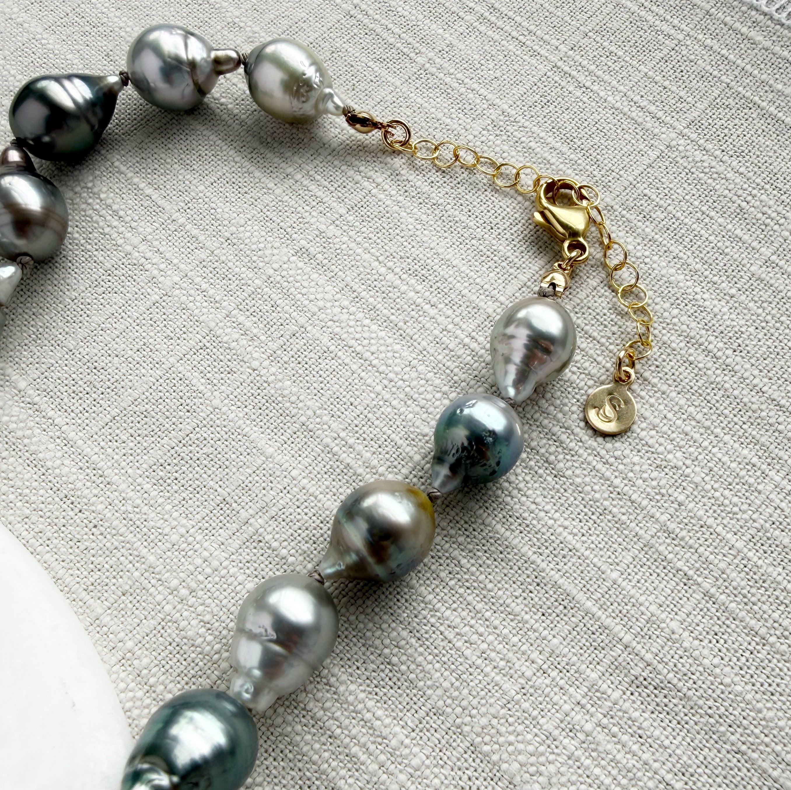 Clasp detail of Tahitian pearl necklace on a marble coaster with a textured beige background