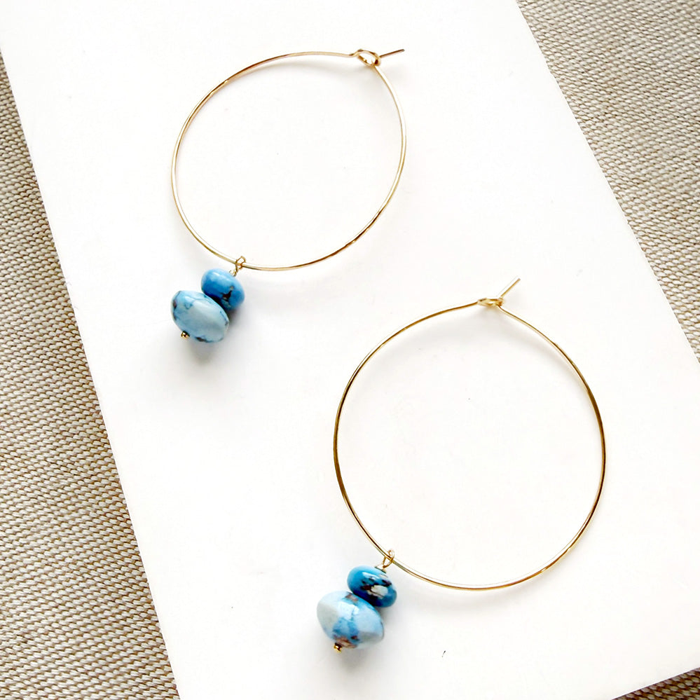 Pair of hoop earrings with small Golden Hills Turquoise beads, displayed on a white card against a textured gray background.