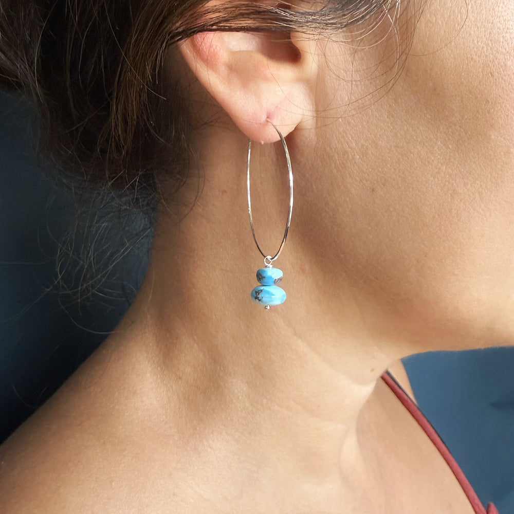 A close-up of a person's ear wearing a silver hoop earring with small Golden Hills turquoise beads dangling from the bottom.