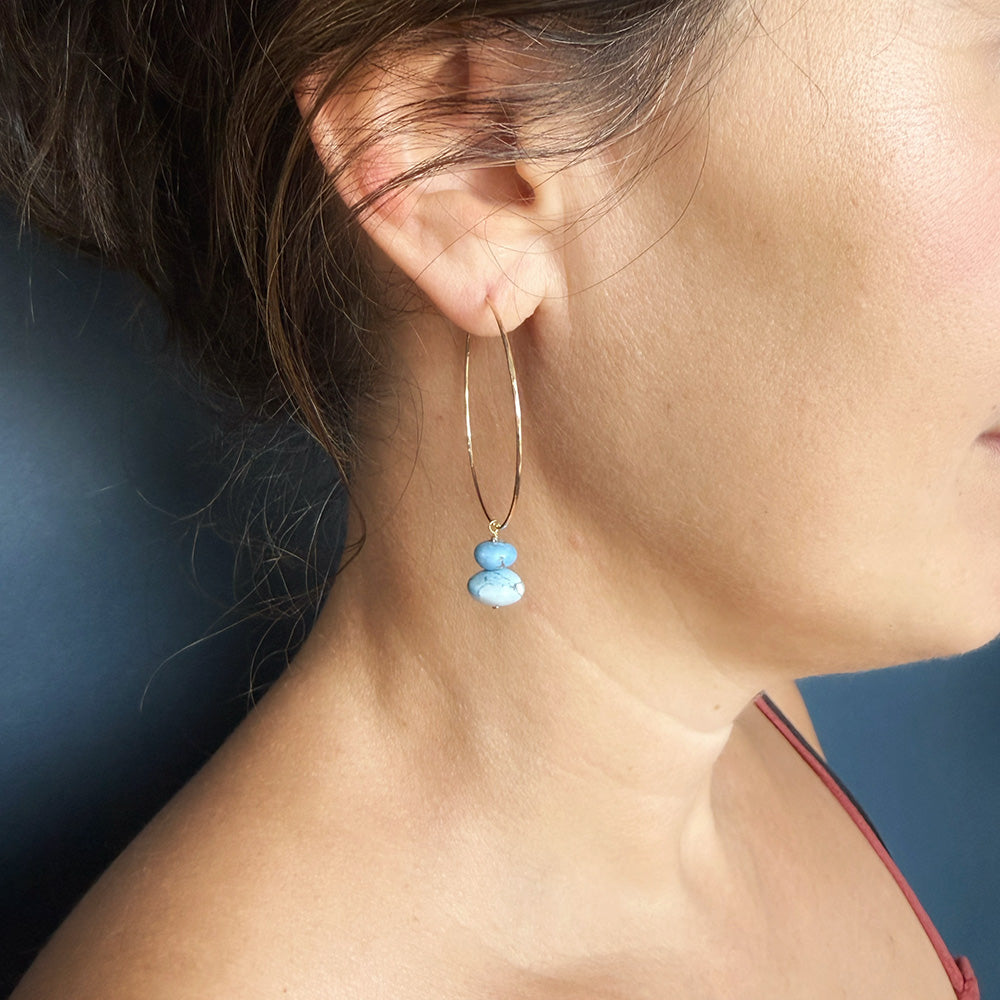 A close-up side profile of a woman wearing a gold hoop earring with two small Golden Hills Turquoise beads dangling from it.