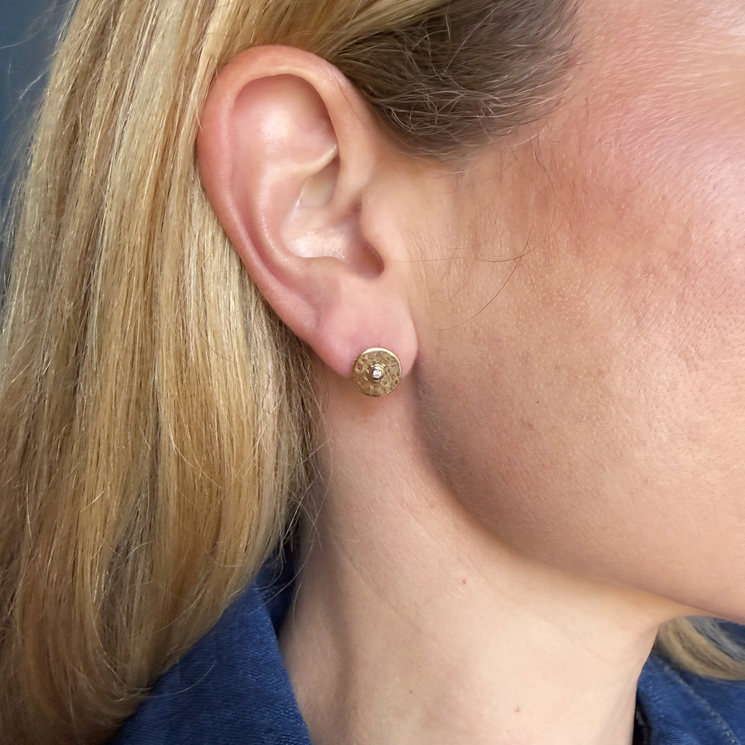 Close-up of a person wearing gold stud earring with a blue shirt.