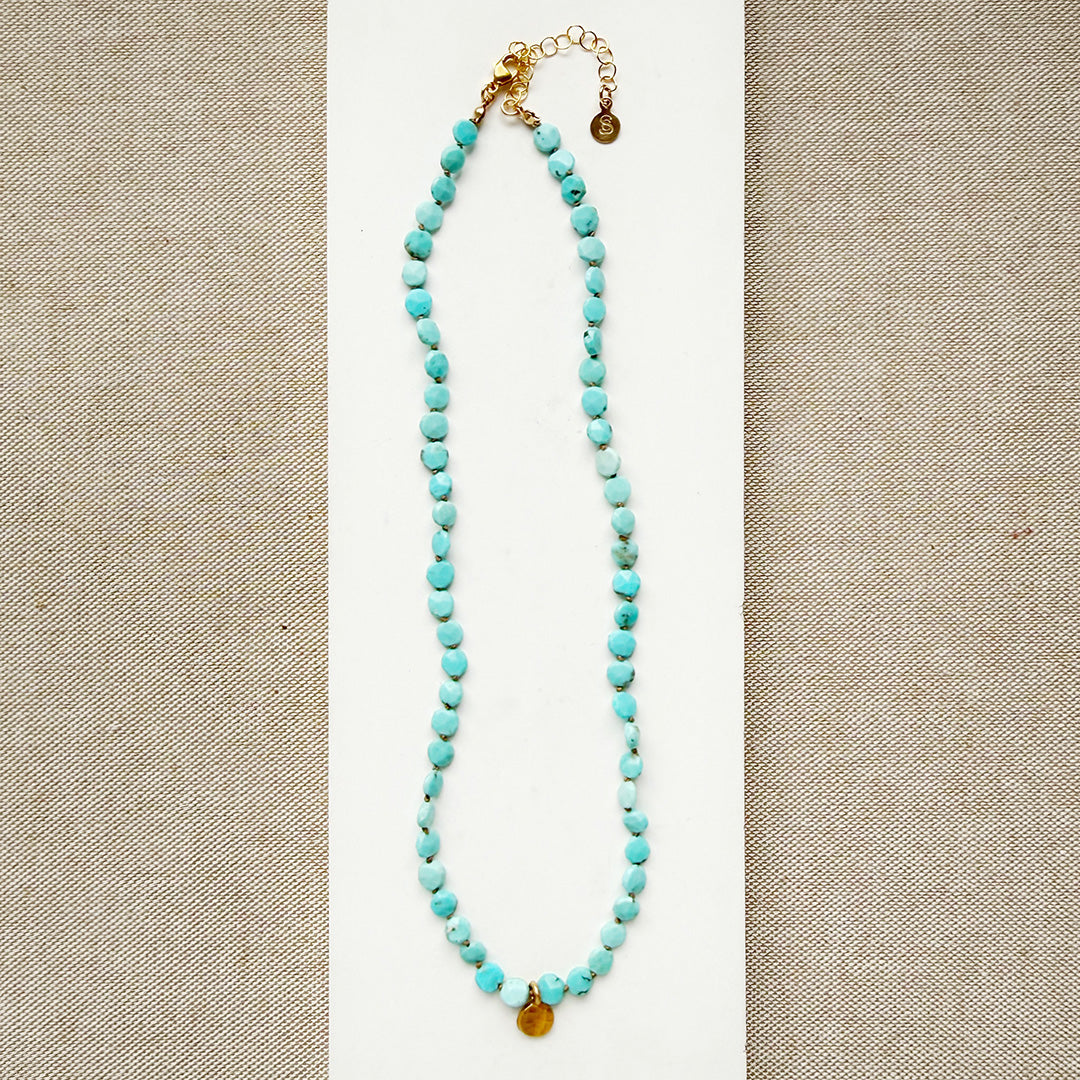 Turquoise beaded necklace with gold accents on a beige background