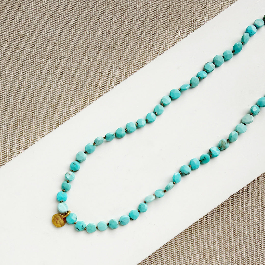 Turquoise beaded necklace with gold accent on a white and beige surface