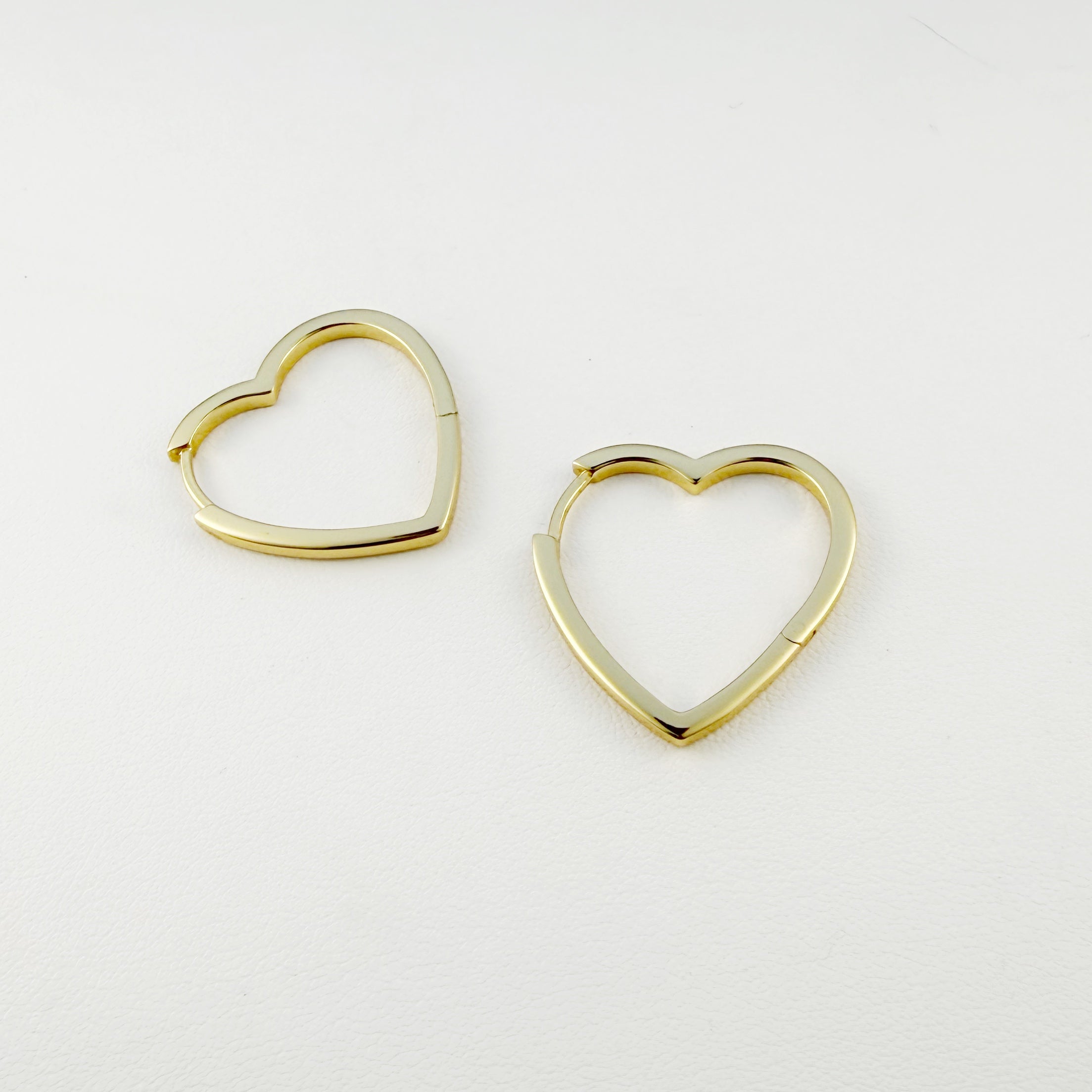Gold heart-shaped hoop earrings on a light gray background