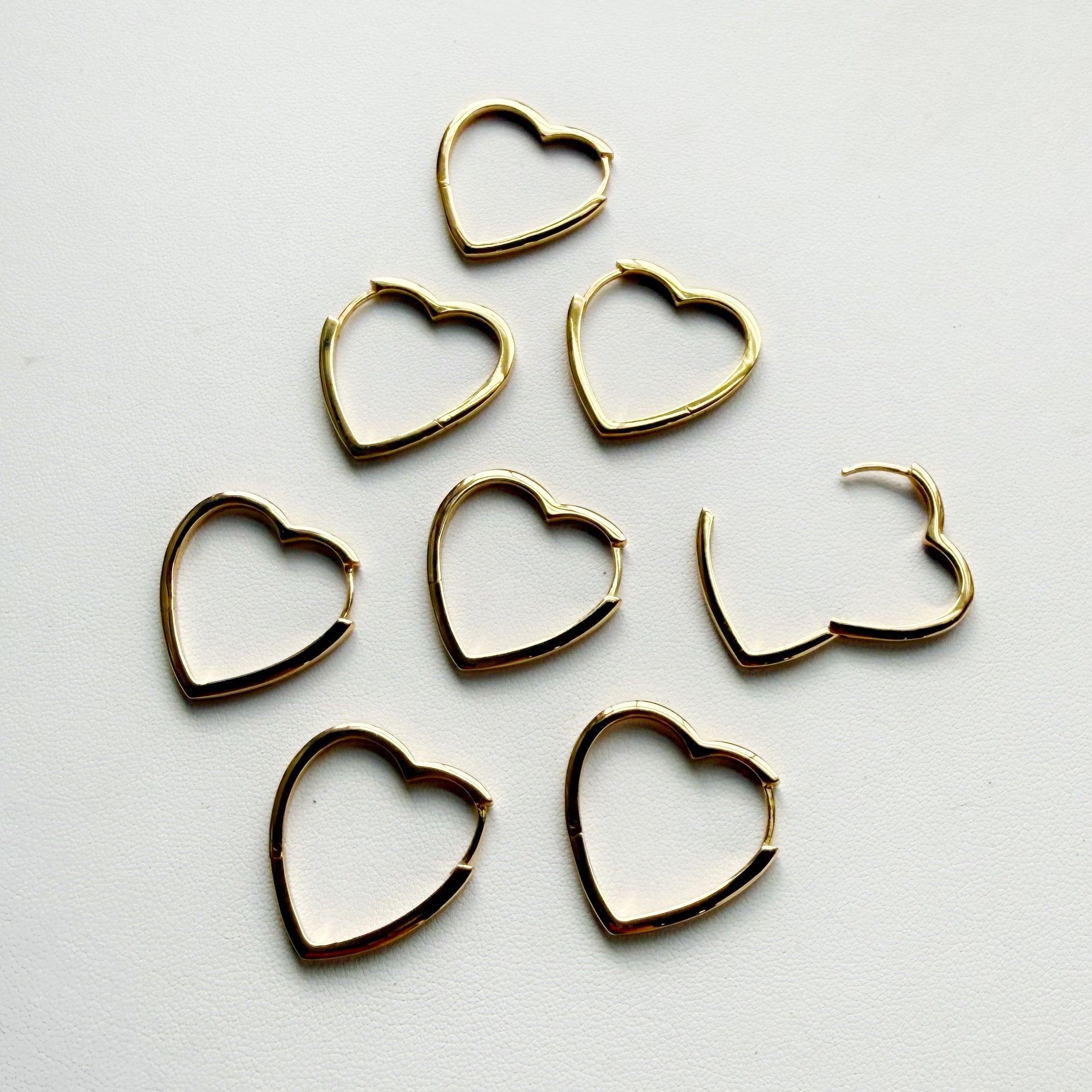 Gold heart-shaped earrings on a light gray background