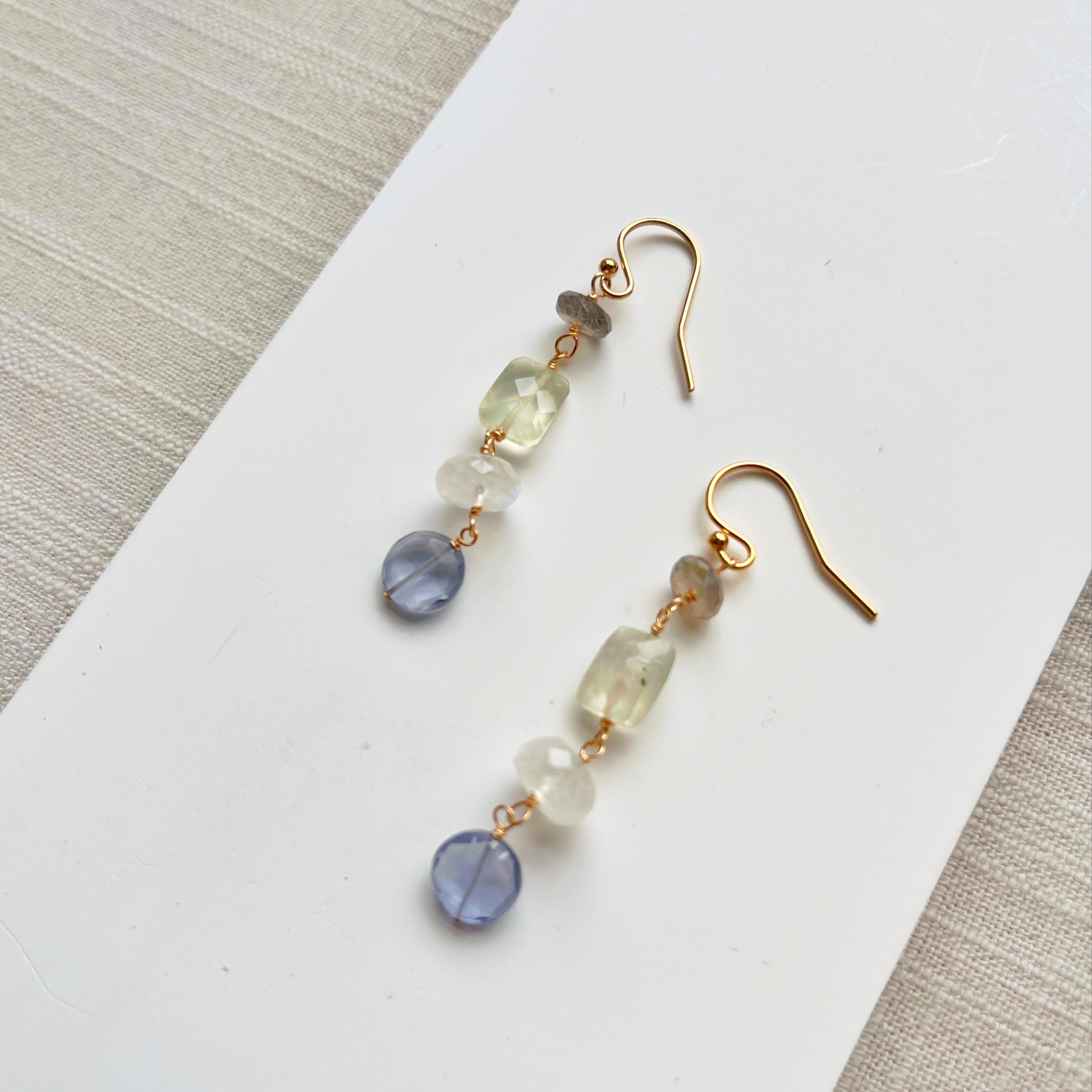 Pair of gold earrings with multicolored beads on a white surface.