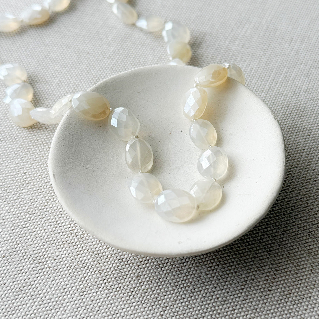 White chalcedony knotted necklace in a white dish with a gray background