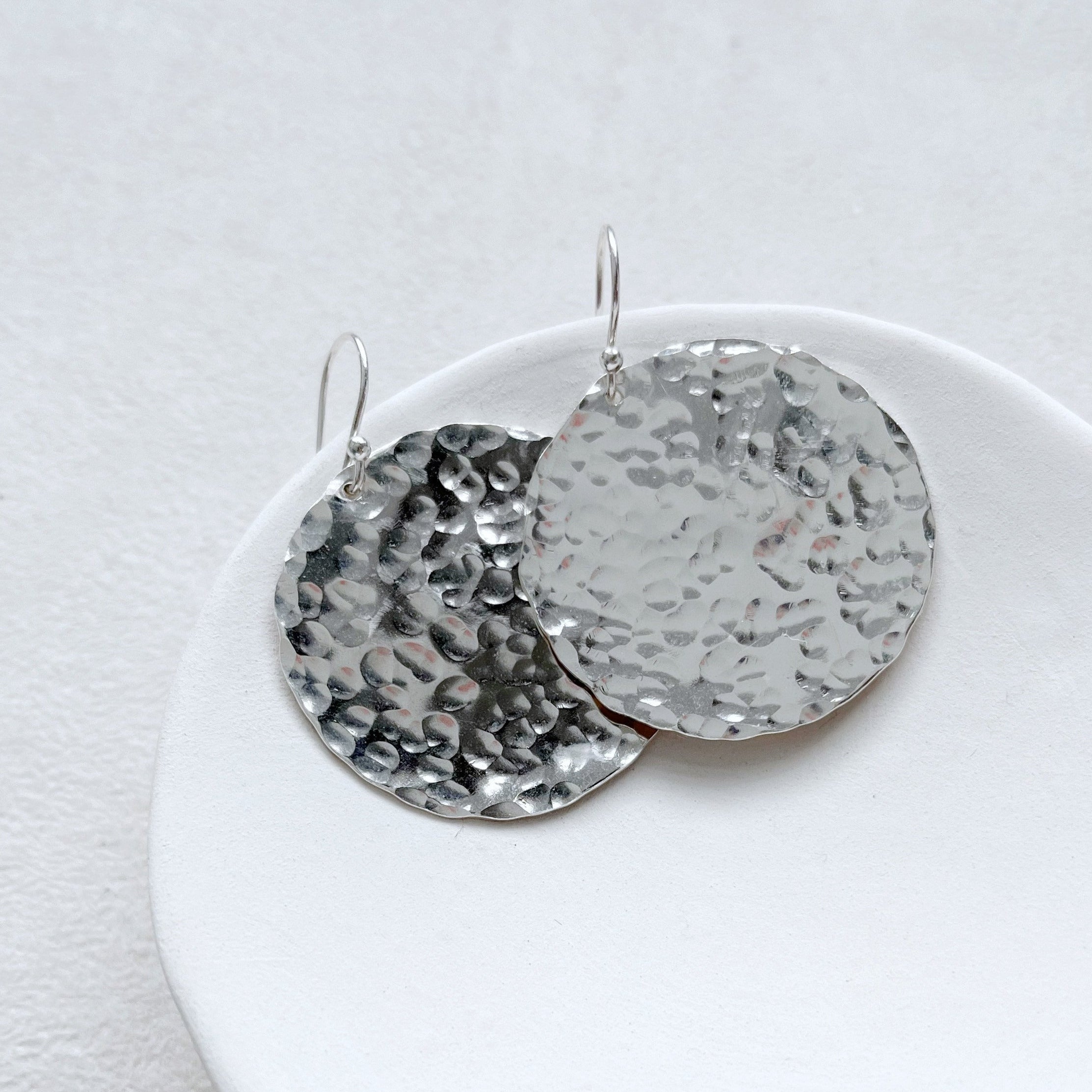 A pair of sterling silver disc earrings with a hammered texture displayed on a white cloth.